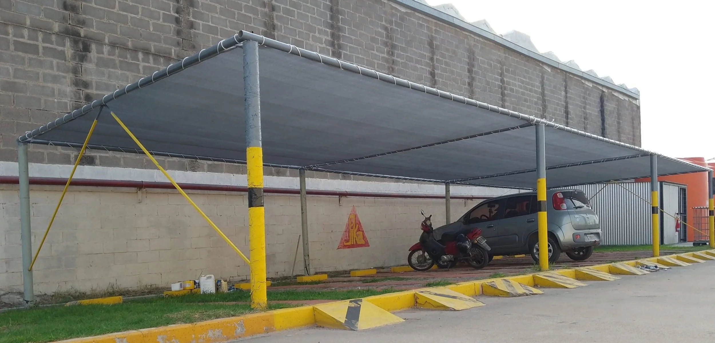 Cochera con mediasombra gris instalada en estructura metálica para estacionamiento, con vehículo bajo la cobertura