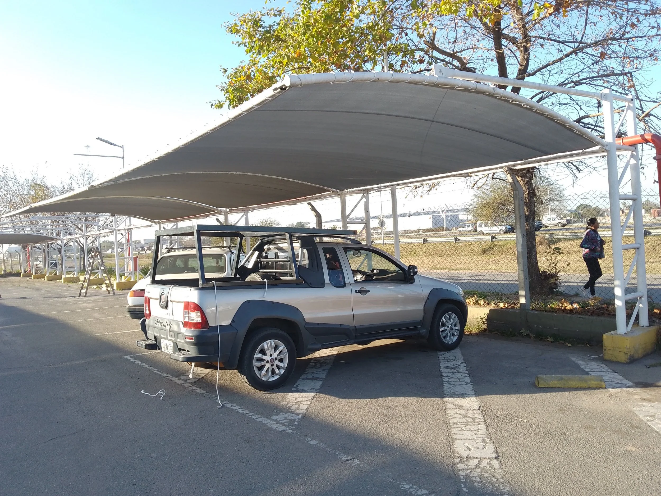 Cochera con mediasombra instalada sobre estructura metálica en estacionamiento, con vehículo bajo la cobertura