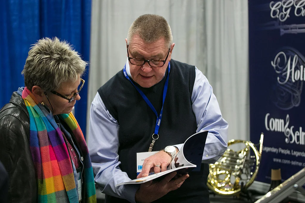 Male exhibitor showing female conference attendee a book for sale in the Illinois Music Education Conference exhibit hall.