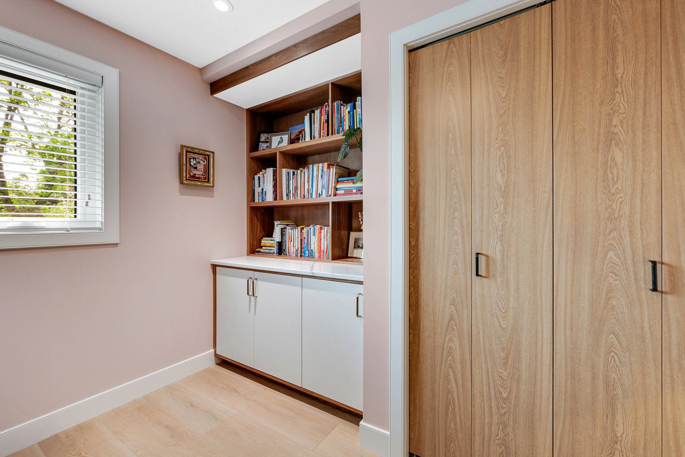 Interior corner of a room with a window, wooden cabinet with books, and a closed wooden closet door.