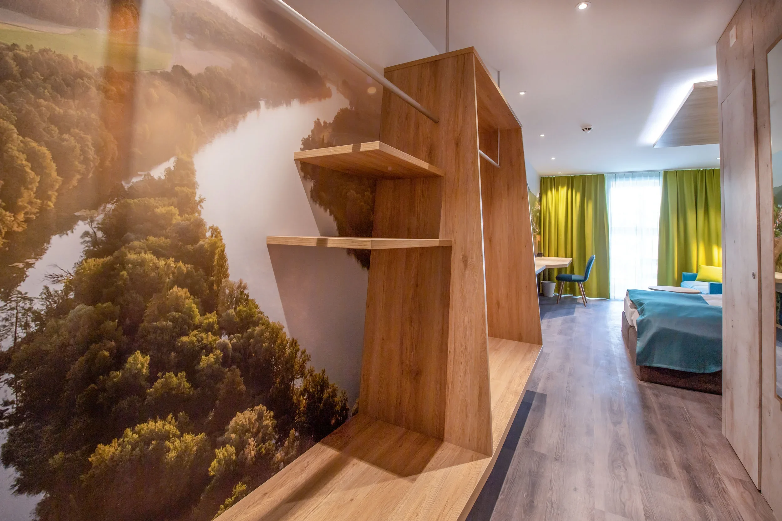 Interior of a modern room with a large wall mural of a forest and river, wooden built-in shelves, and green curtains across a window.