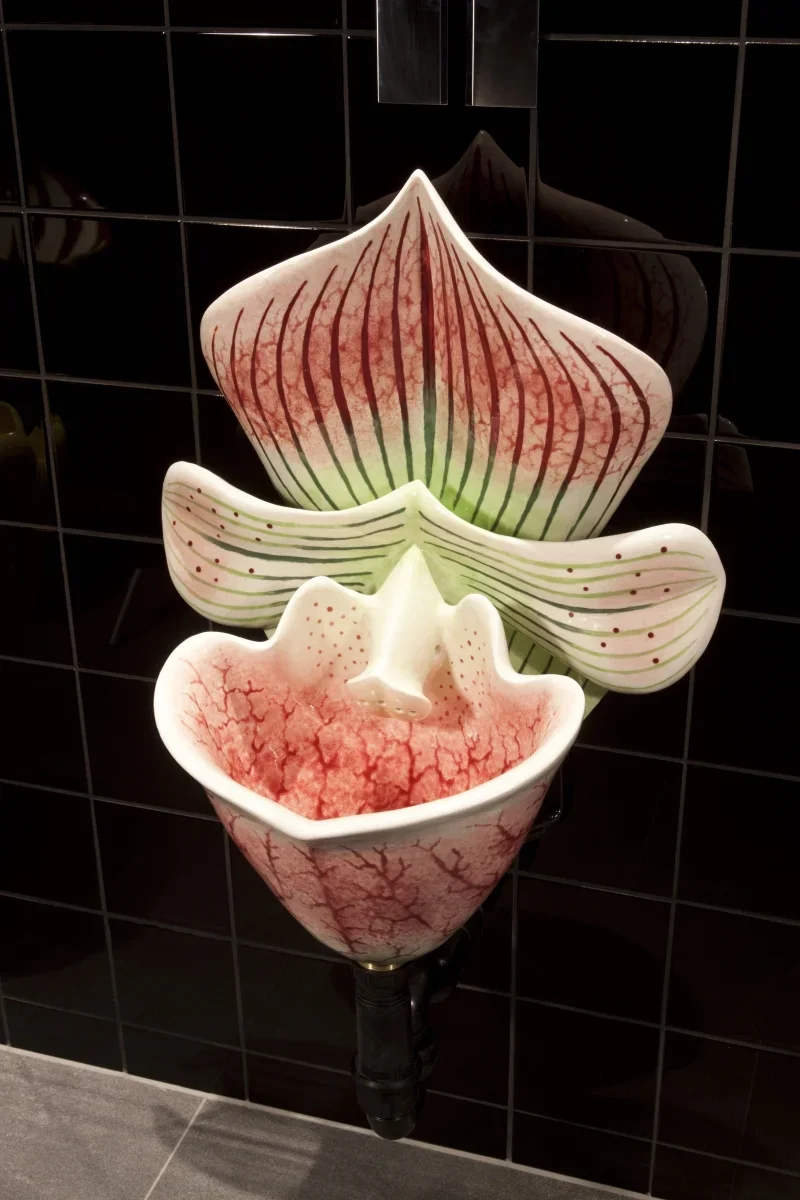 Decorative ceramic fountain with abstract flower design in red, white, and green, mounted on a black tiled wall.