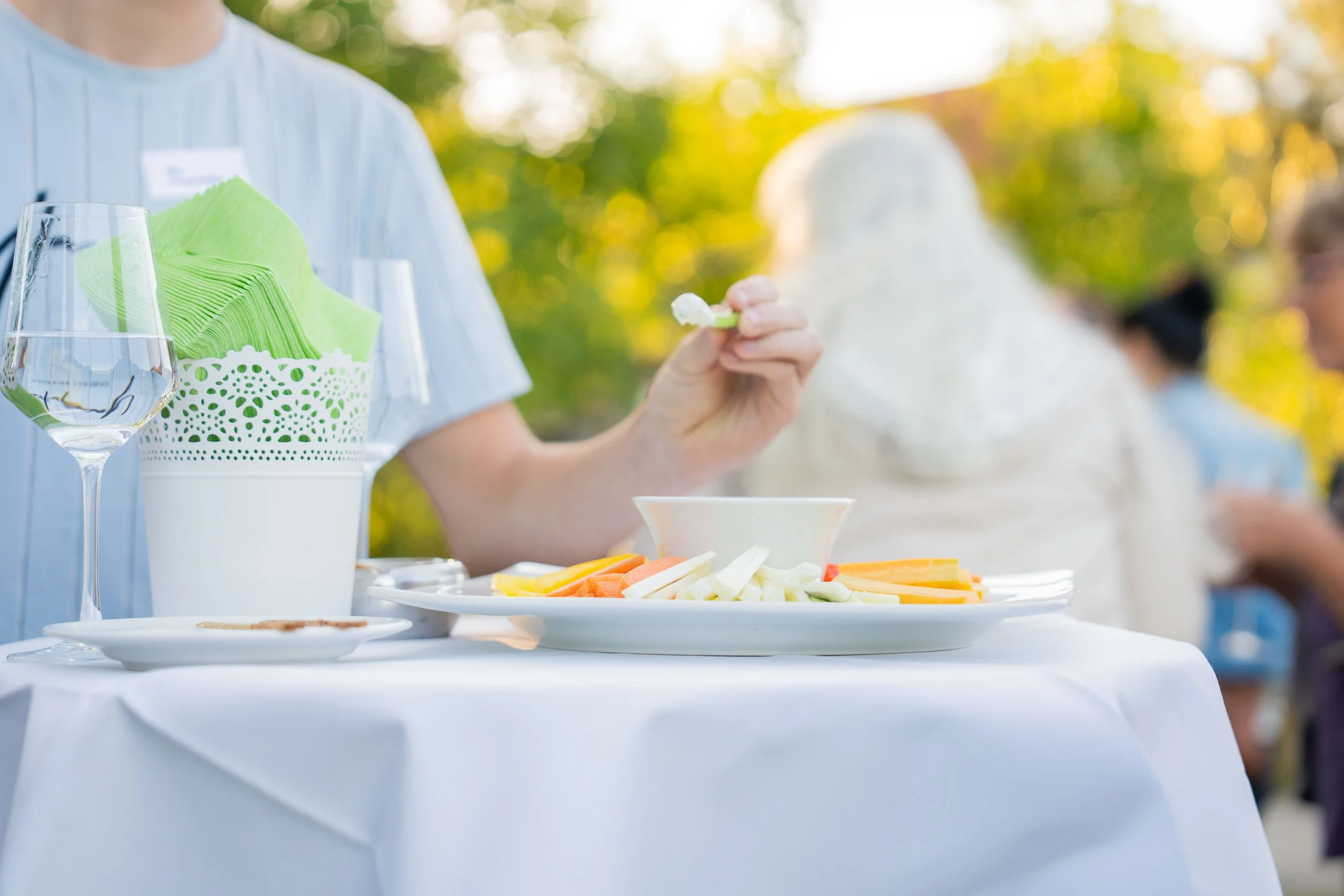 Person richtet belegte Brote auf einer Platte bei einem Buffet. Im Hintergrund sind Weingläser und dekorative Gegenstände sichtbar.