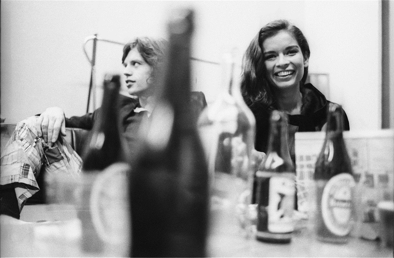 © Henry Diltz, 1970 Backstage after a Rolling Stones concert in Amsterdam on October 9, 1970. Henry was trying to photograph Mick through the bottles on the table so he wouldn't notice. "Some girl next to him kept watching me and smiling, which made it hard for me to hide what I was doing. Later I learned she was his girlfriend, Bianca." -Henry Diltz