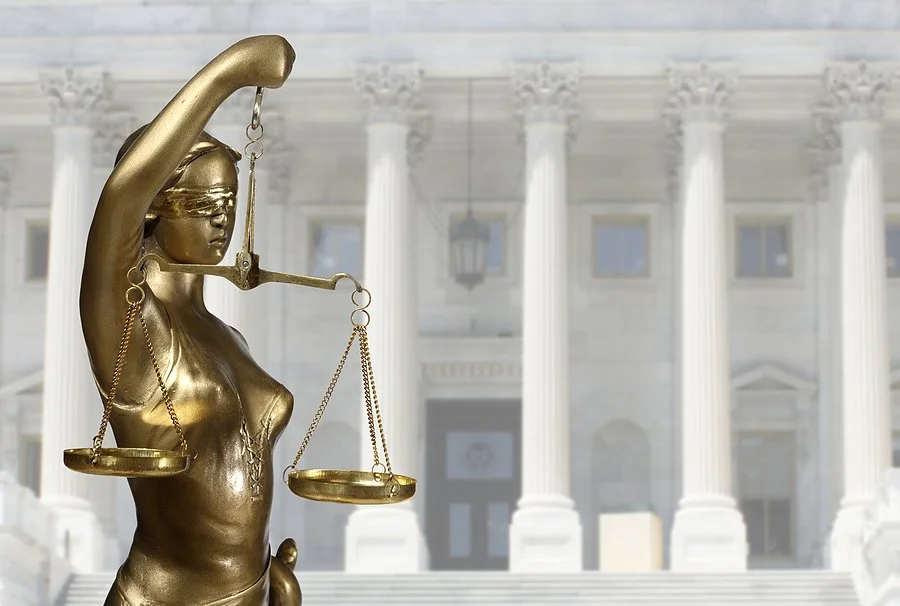 A statue of Lady Justice holding balanced scales stands in front of a courthouse.