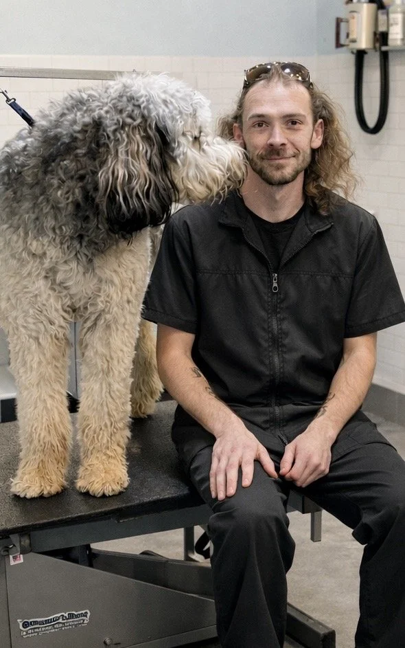 A man sitting on a veterinary examination table with a fluffy, curly-haired dog next to him in a clinic room.