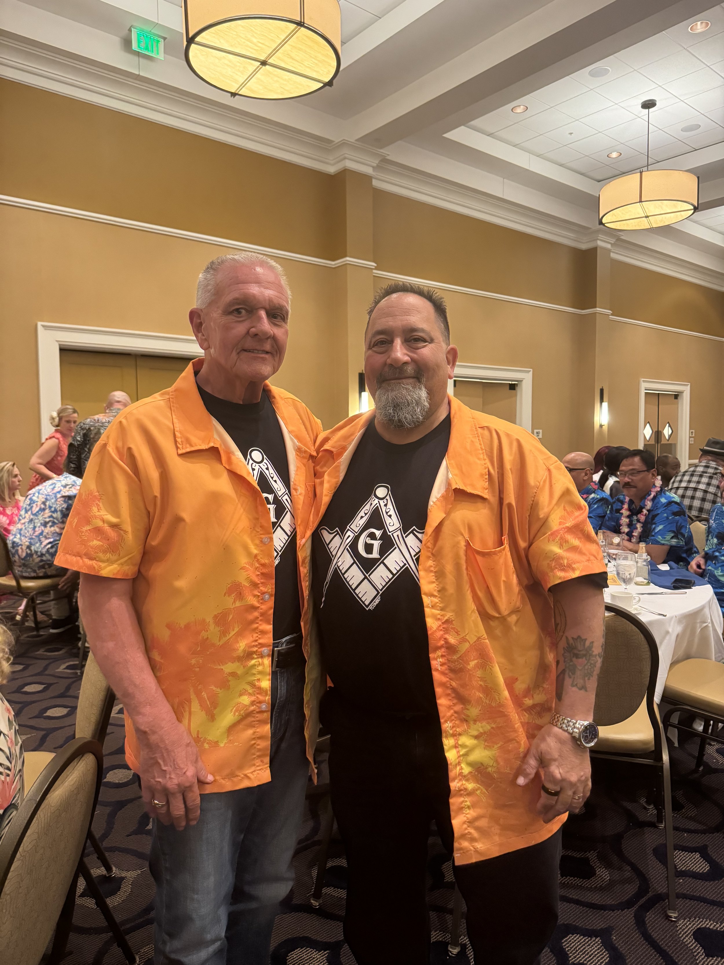 RWB Angelo Deserio and MW PGM Anthony R. Cracco, Illinois Freemasons, in black t-shirts adorned with the Masonic square and compasses, with an orange button-down shirt layered on top