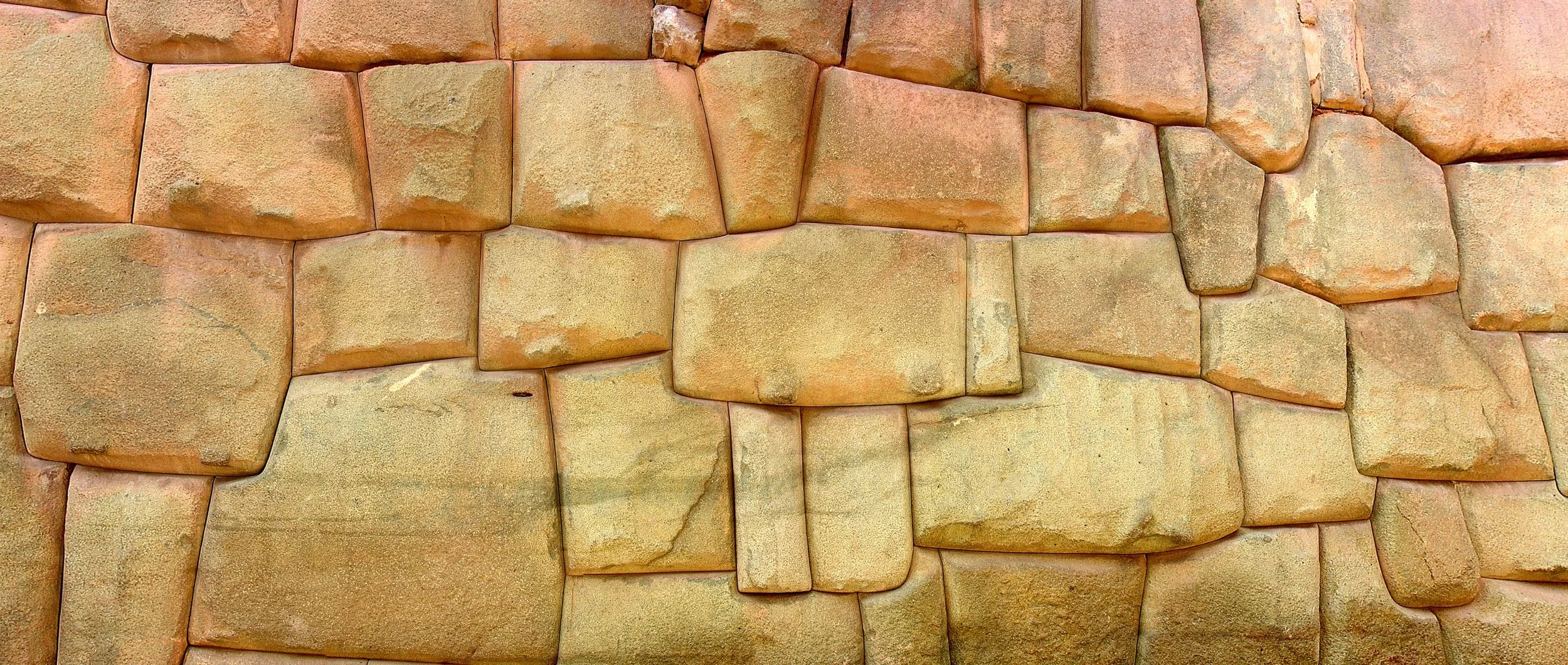 A close-up of an Inca ashlar masonry wall in Cuzco, Peru, showing precisely fitted irregular stone blocks in warm sandstone tones.