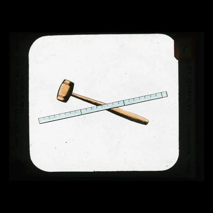 Masonic magic lantern slide showing Masonic tools, ruler and mallet. Pale blue border imprinted with: "...lley Company, Columbus, Ohio / Take hold with thumb on star and place/slide in carrier.