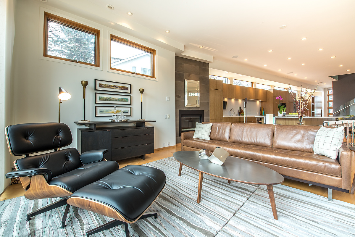 The modern style furniture in this living room features an authentic Herman Miller Eames Lounge Chair and complimentary warm colours. Neutral greys keep the space feeling up-to-date, and smooth the transition between the living room and more contemporary styled kitchen.