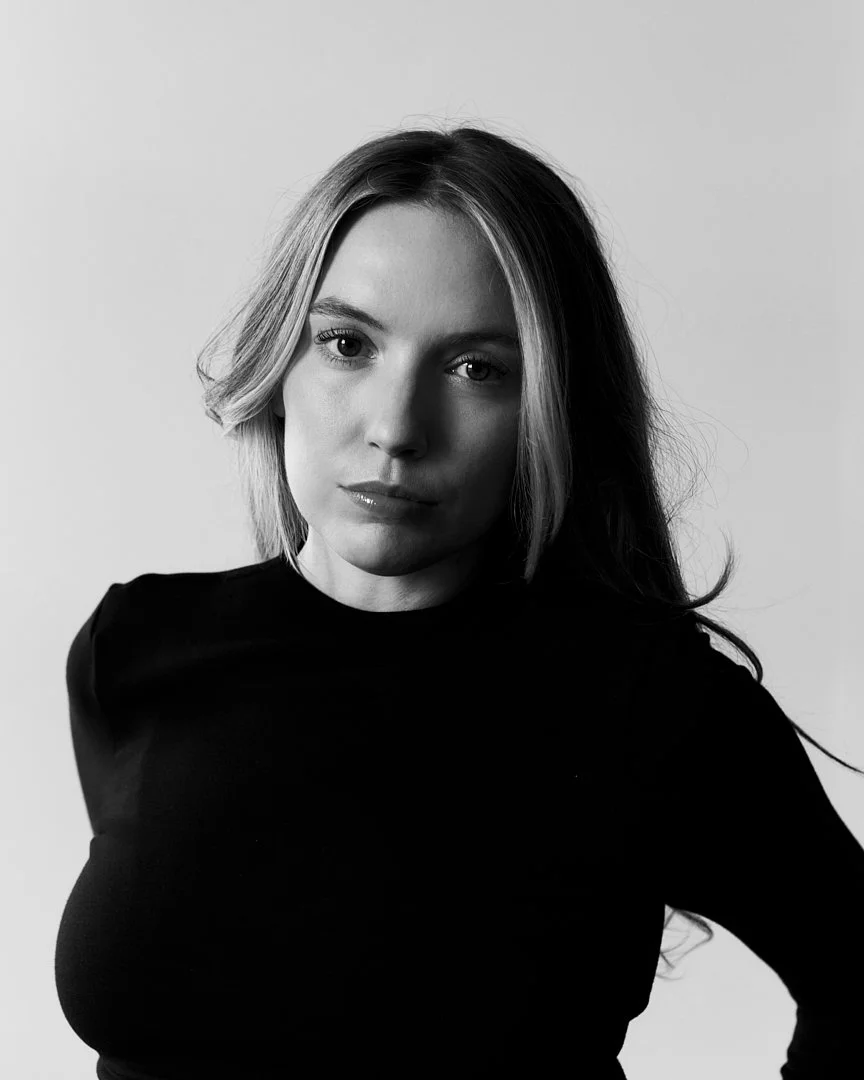 Black and white portrait of a woman with long hair, wearing a dark top, looking directly at the camera with a neutral expression.