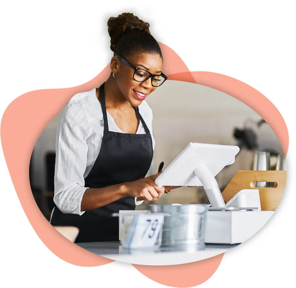 Female restaurant owner wearing a white shirt and black apron entering information into her POS system