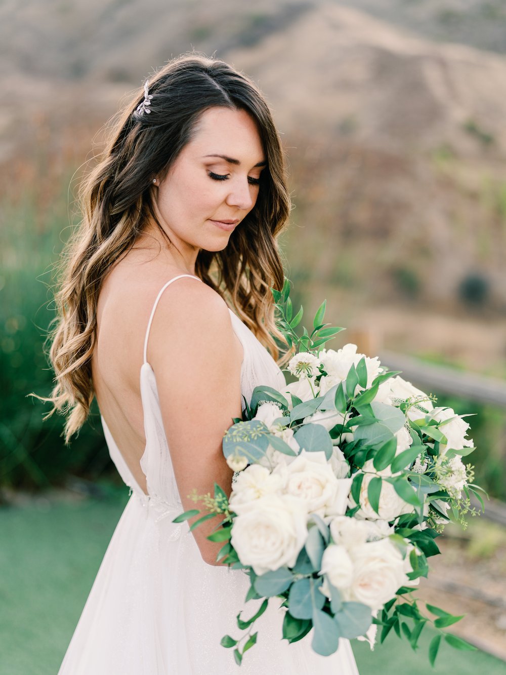 Bride wearing a spaghetti strap wedding dress holding an oversized white floral bouquet.