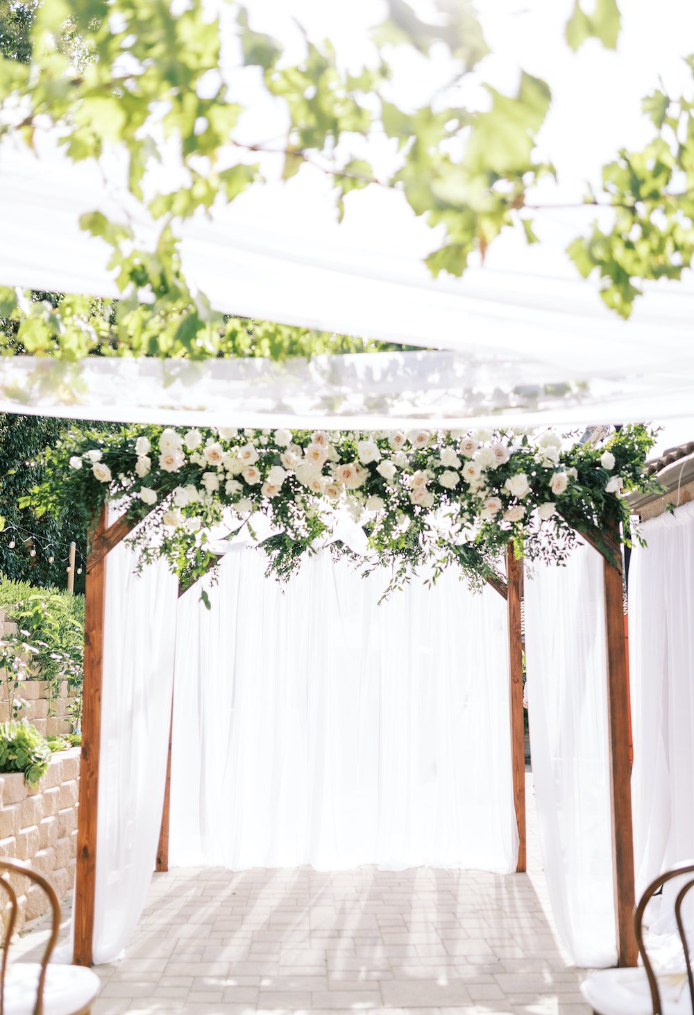 Backyard wedding ceremony chuppah arch with draping and flowers.