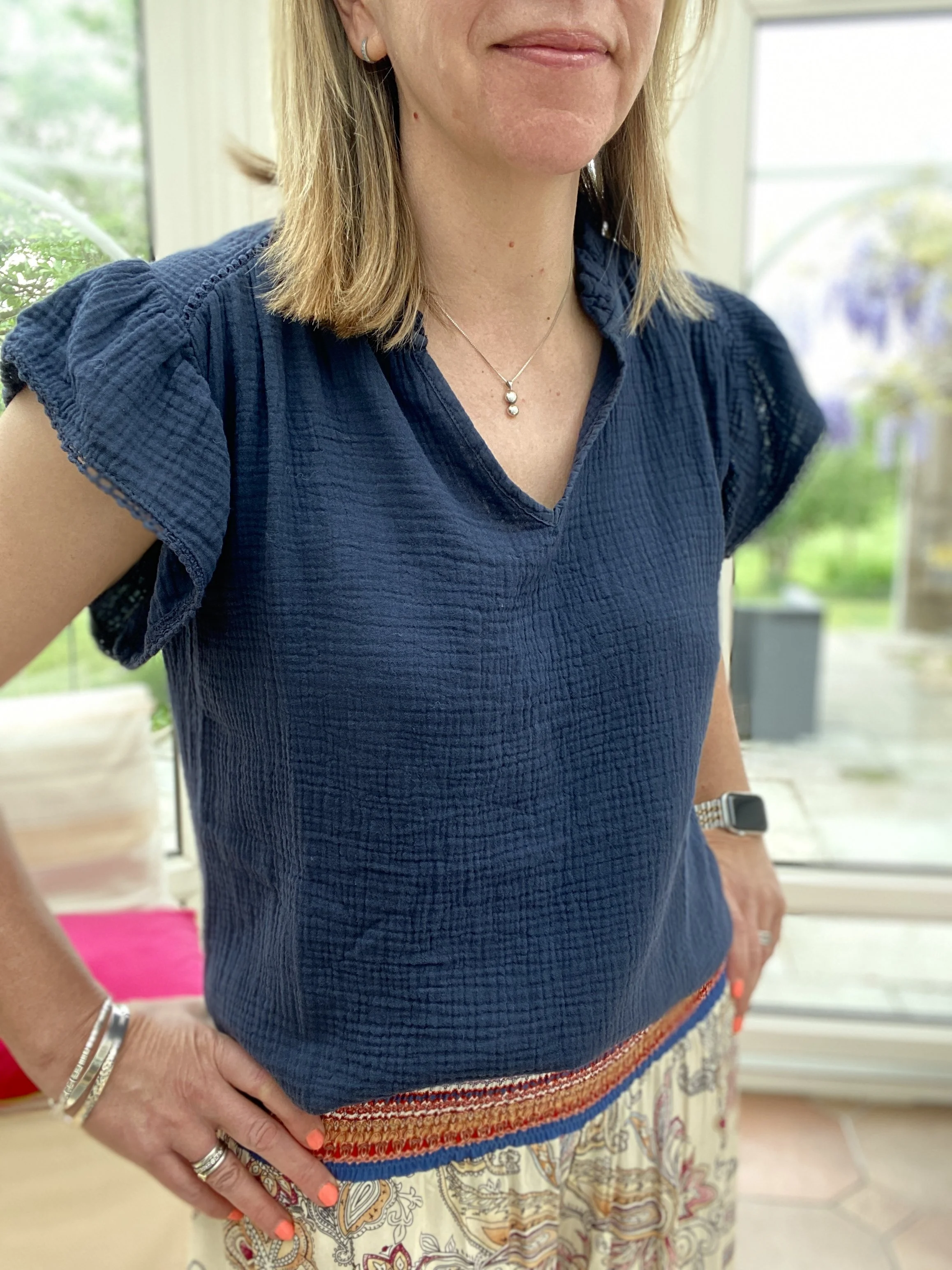 model wearing navy blue short sleeve cotton top which has frill sleeves and an open neckline with frilly collar detail