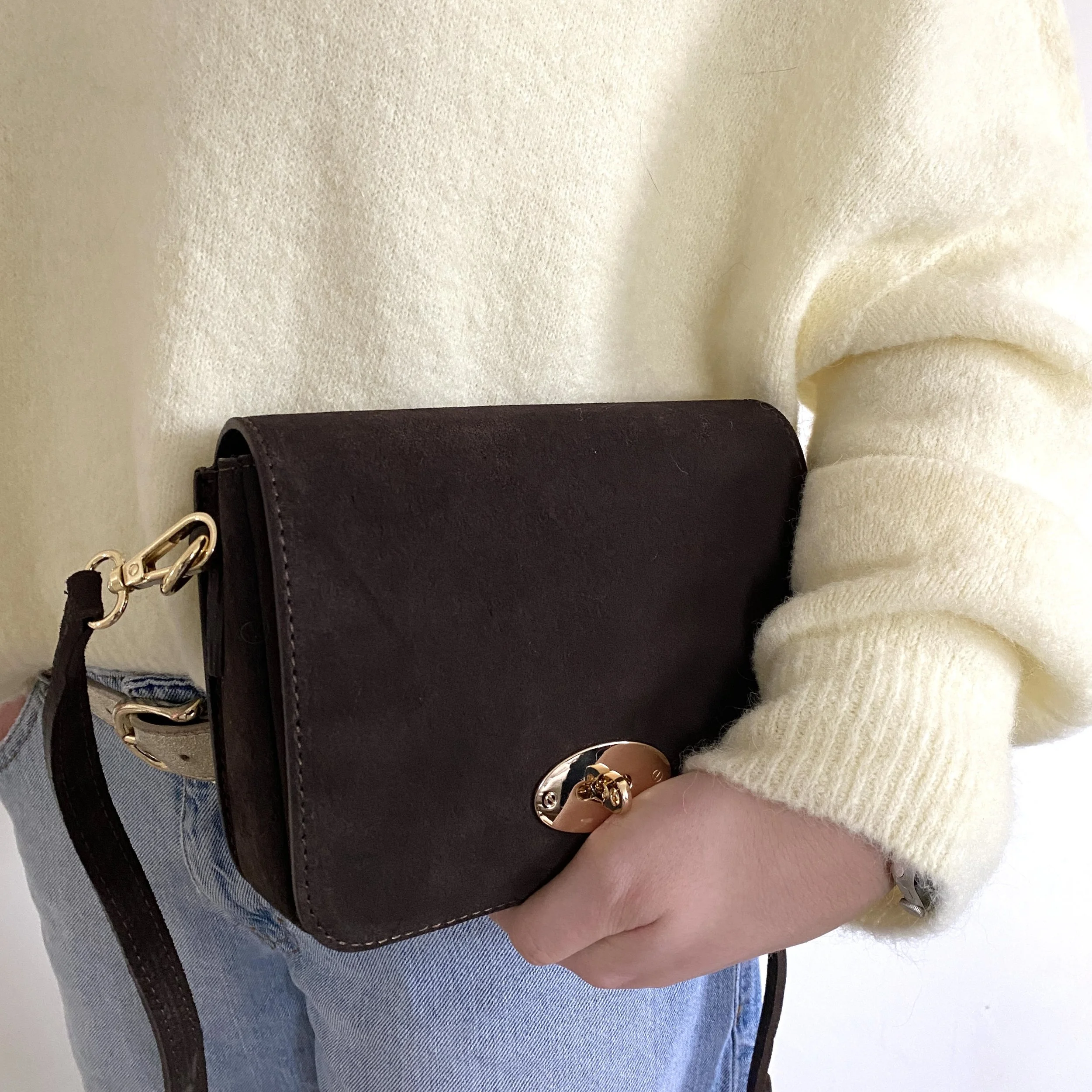 Suede bag with gold clasp being held by model in yellow jumper