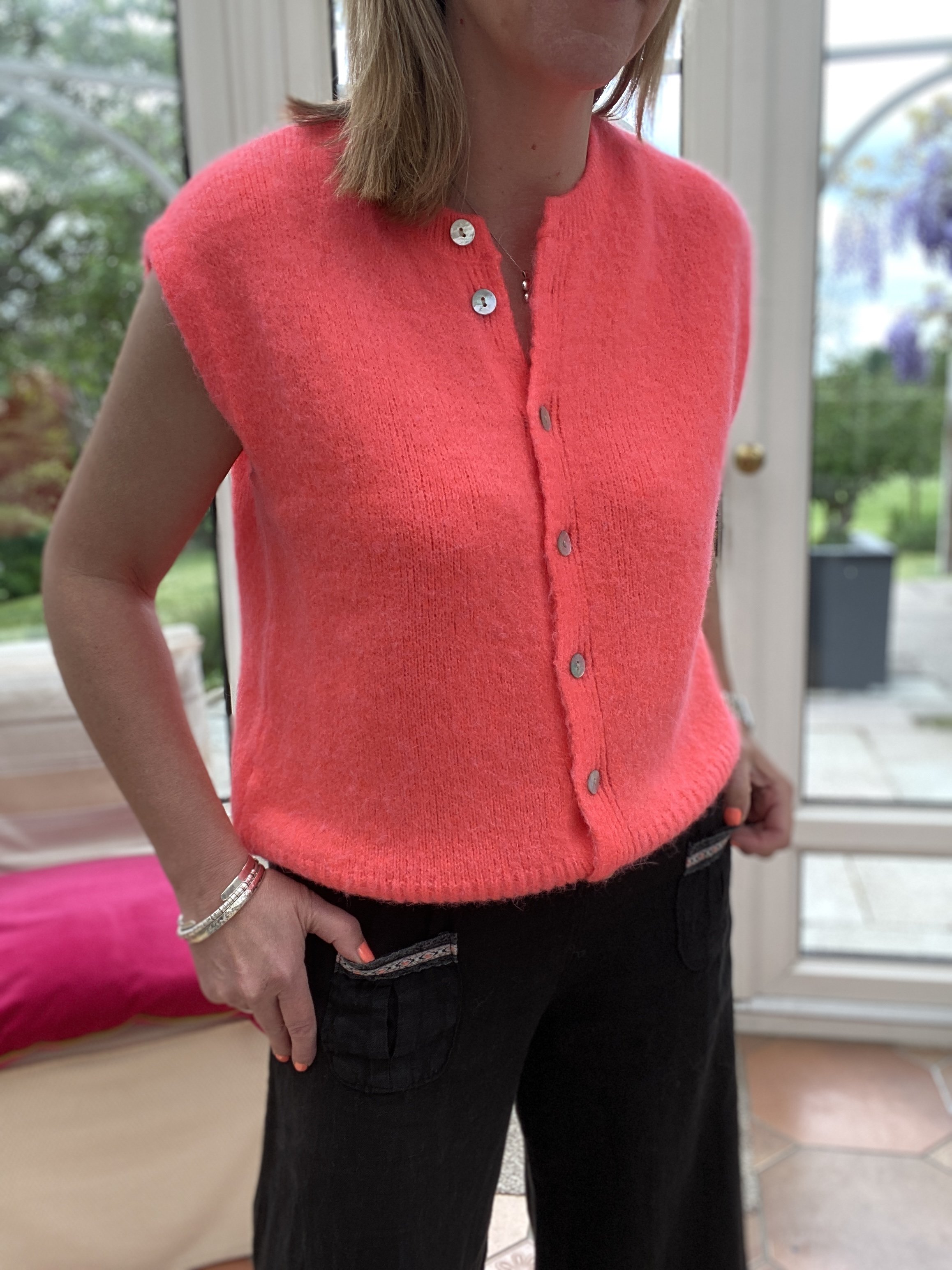 model wearing neon coral sleeveless cardigan with black linen trousers