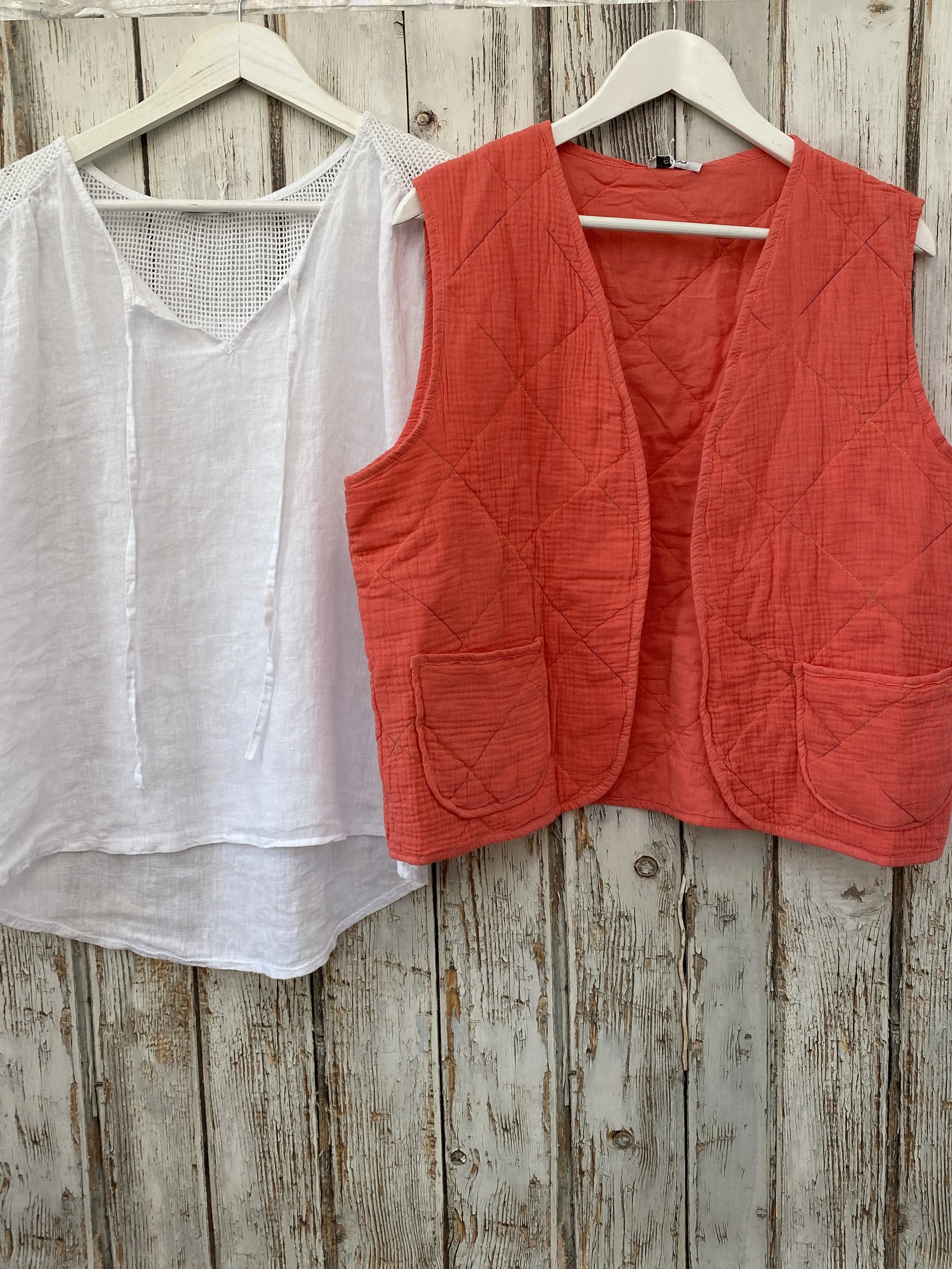 wite linen short sleeve ladies top with a coral coloured quilted gilet on hangers