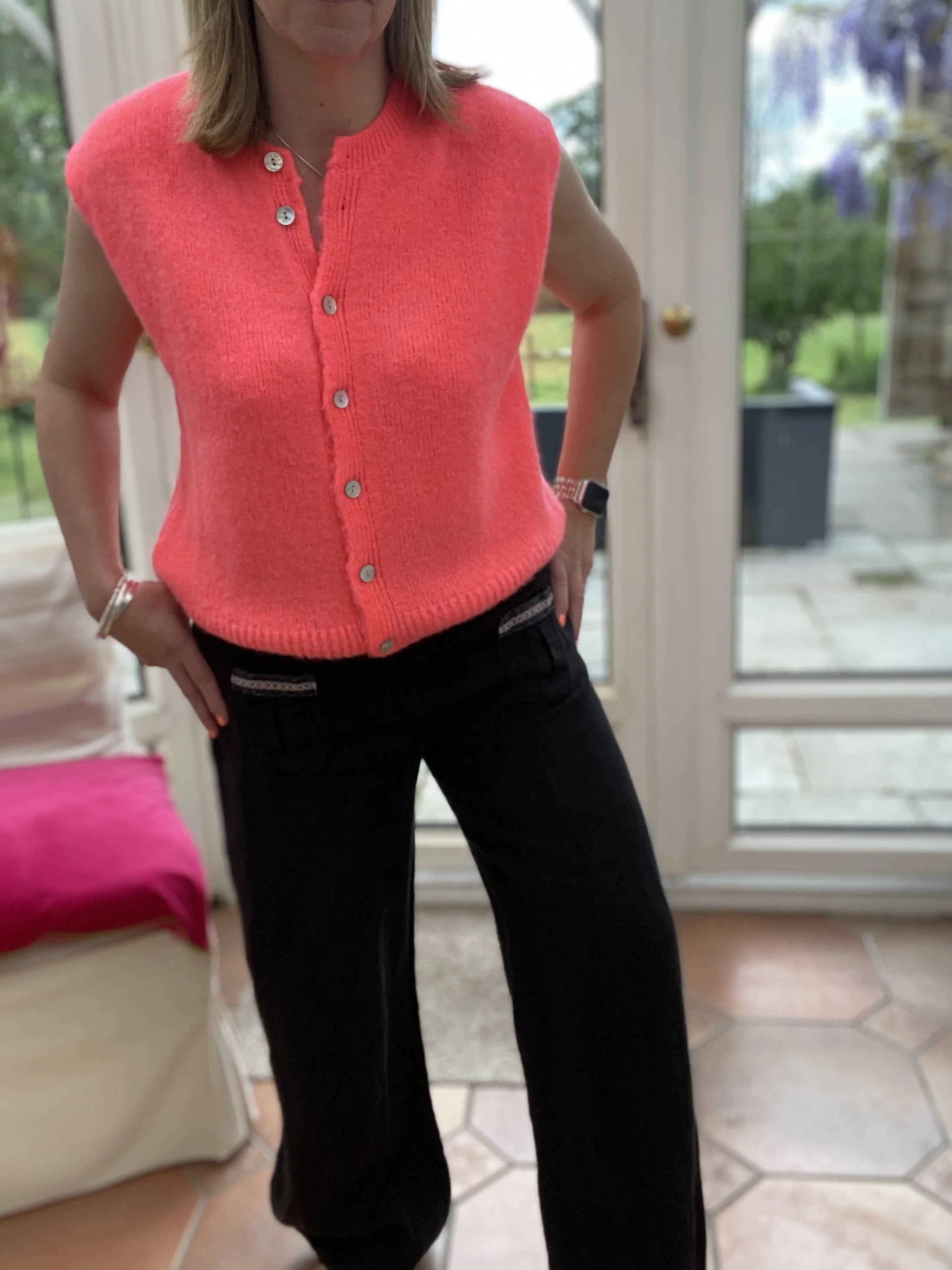 model wearing neon coral knitted vest top with black linen trousers