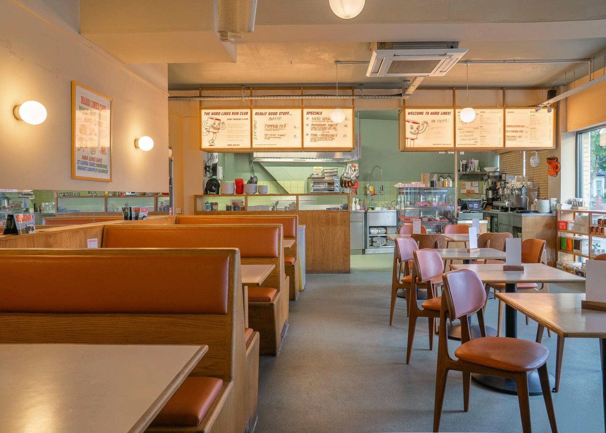 Empty casual restaurant with booths and tables, menu boards hanging above the counter, and large window on the right letting in natural light.
