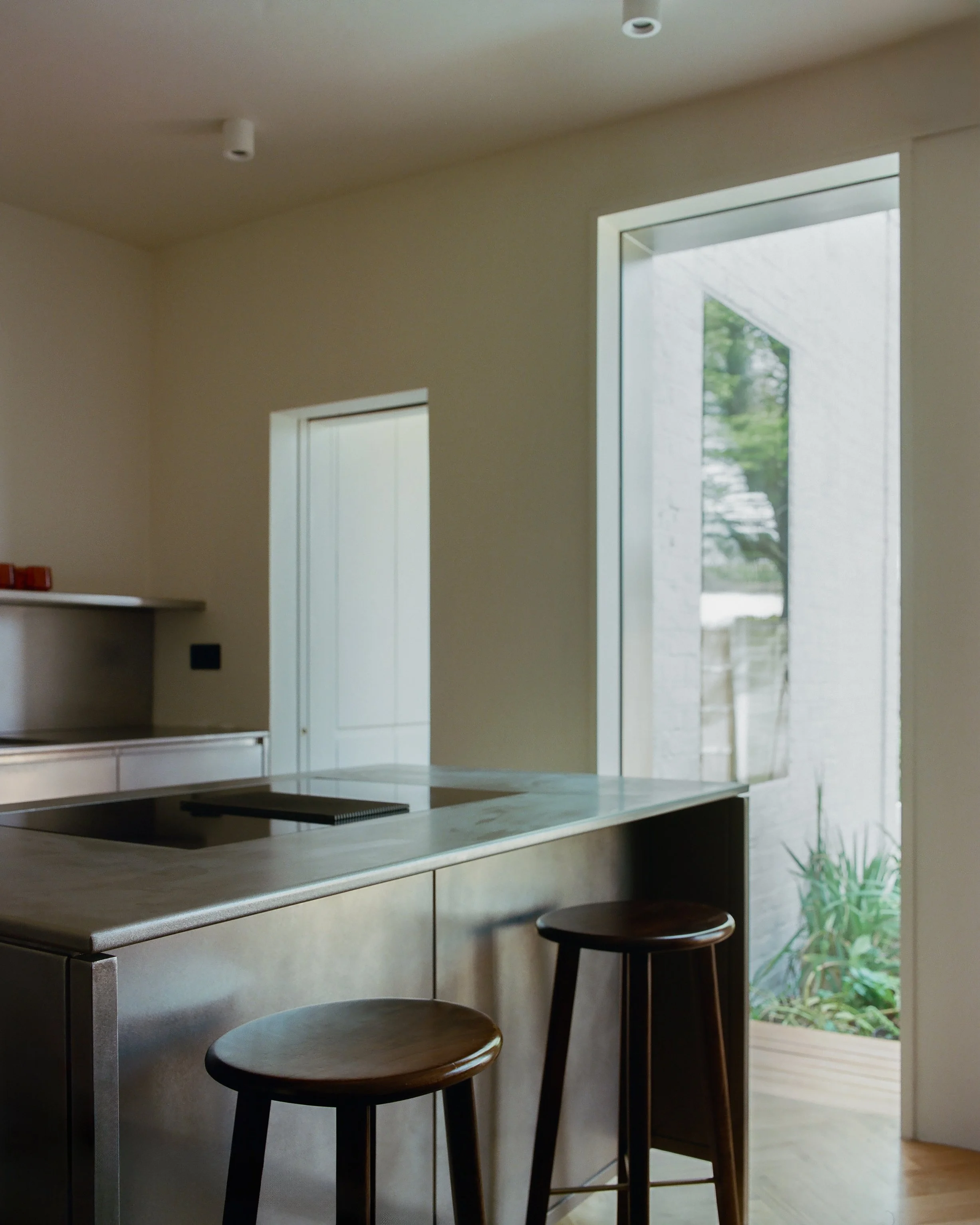 Modern kitchen with a marble island, two wooden stools, large glass door leading outside, and minimal decor.