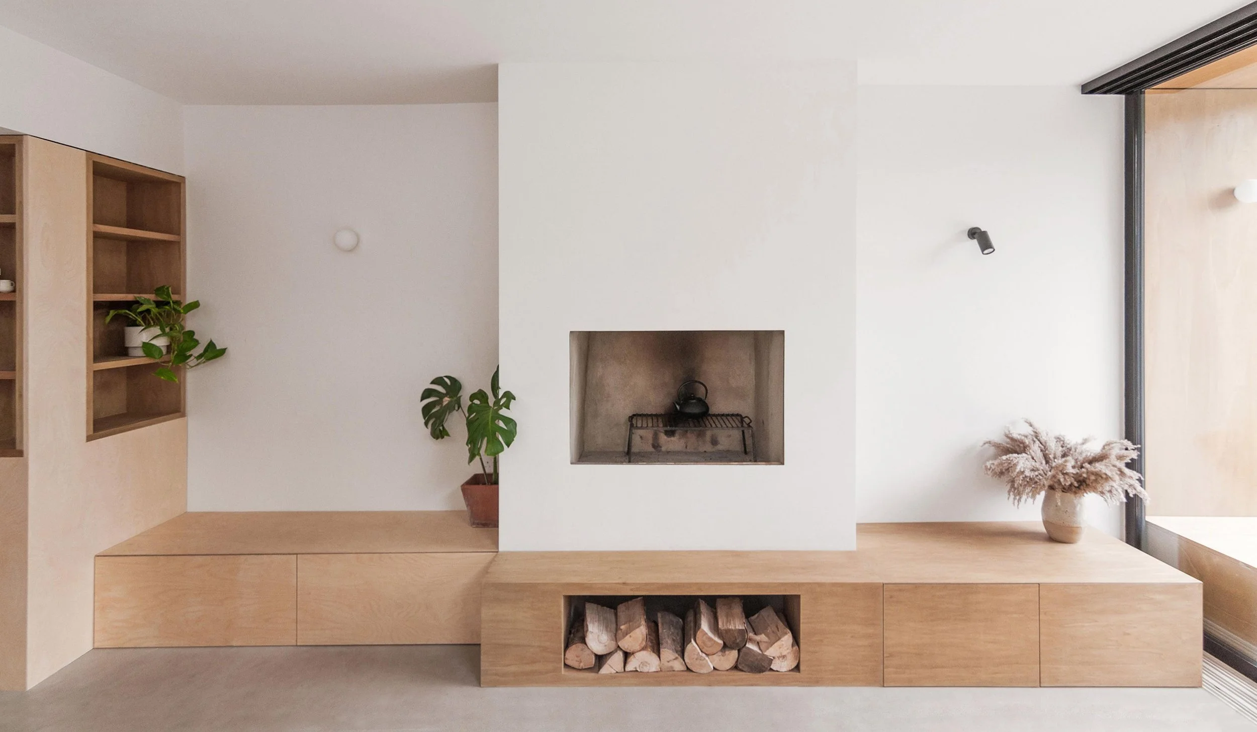 Minimalist living room with a white fireplace, wood storage, and decorative plants.