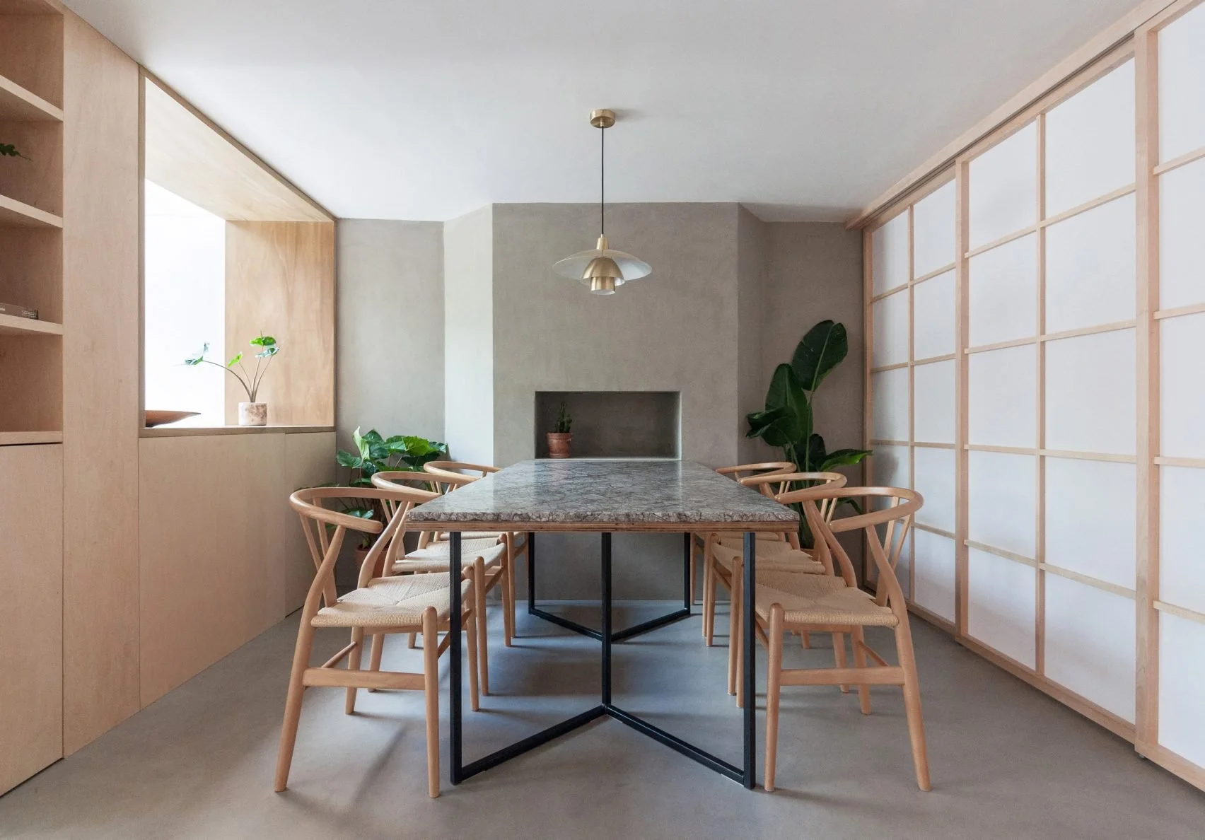 Minimalist dining room with wooden chairs around a marble-topped table, potted plants, and a pendant light.