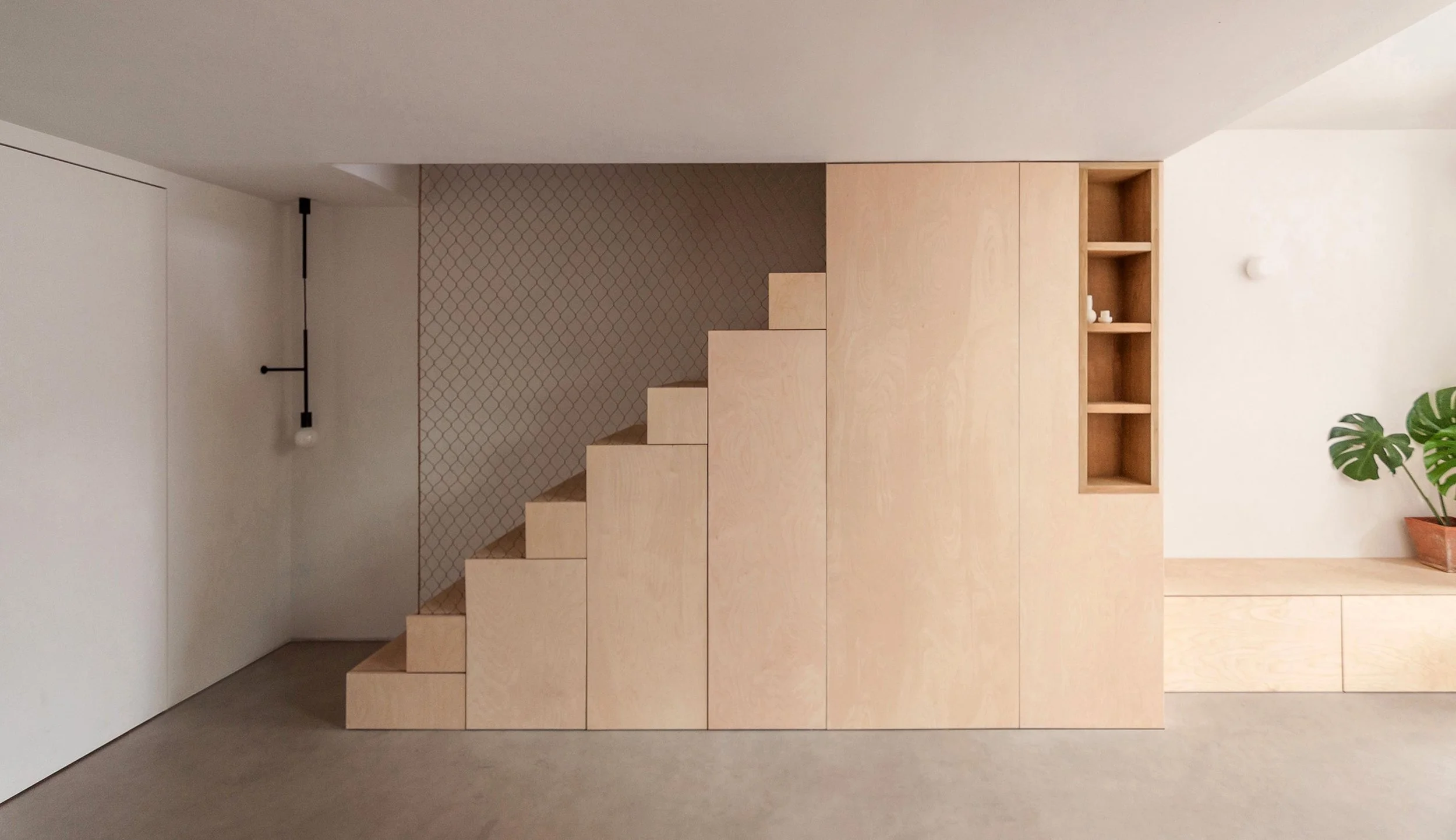 Minimalist interior with light wood stairs, built-in storage, a potted plant, and a modern hanging light fixture.