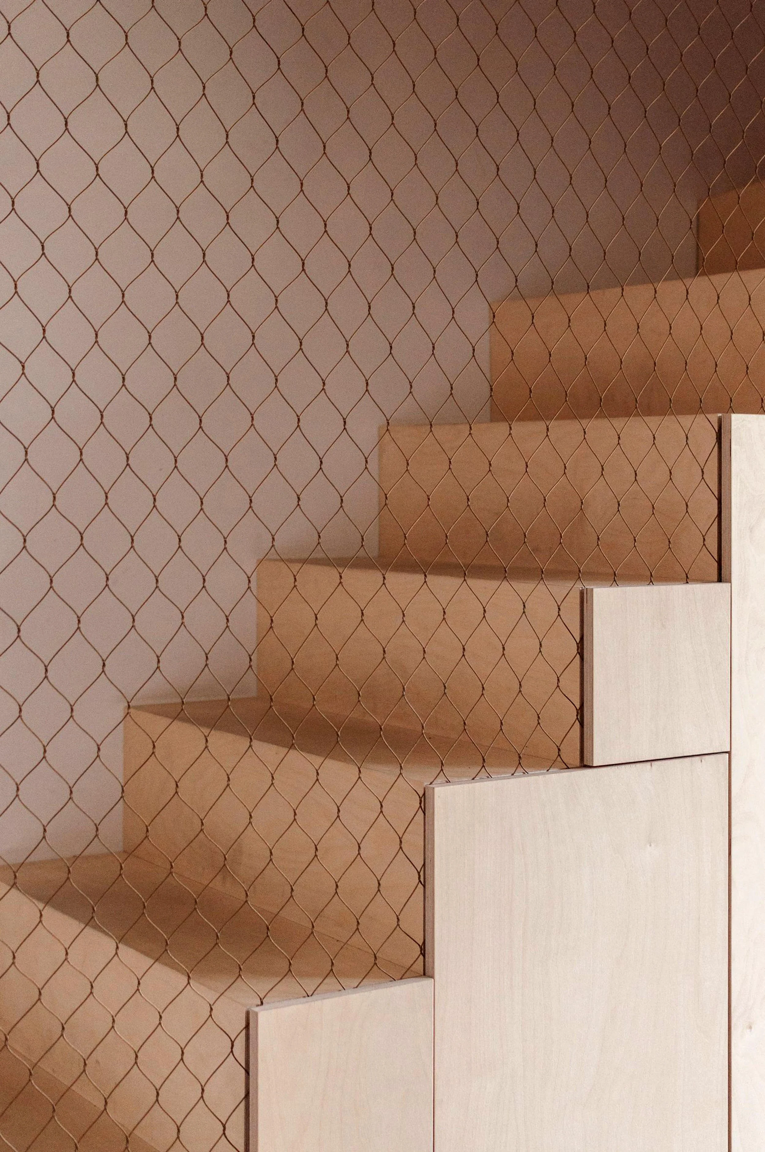 Wooden staircase with triangular steps viewed through wire mesh.