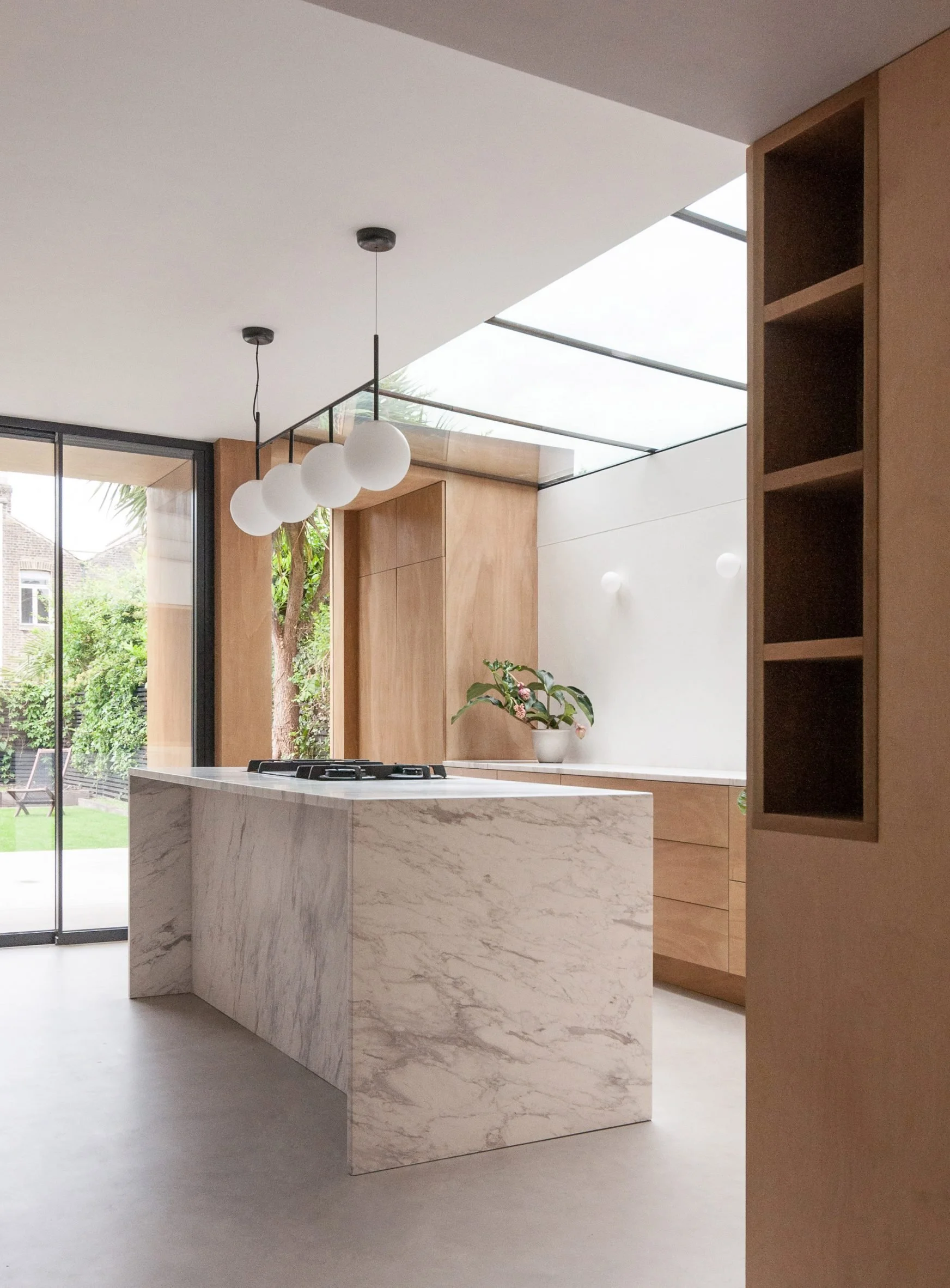 Modern kitchen with white marble island, wooden cabinets, and large glass sliding doors leading to garden