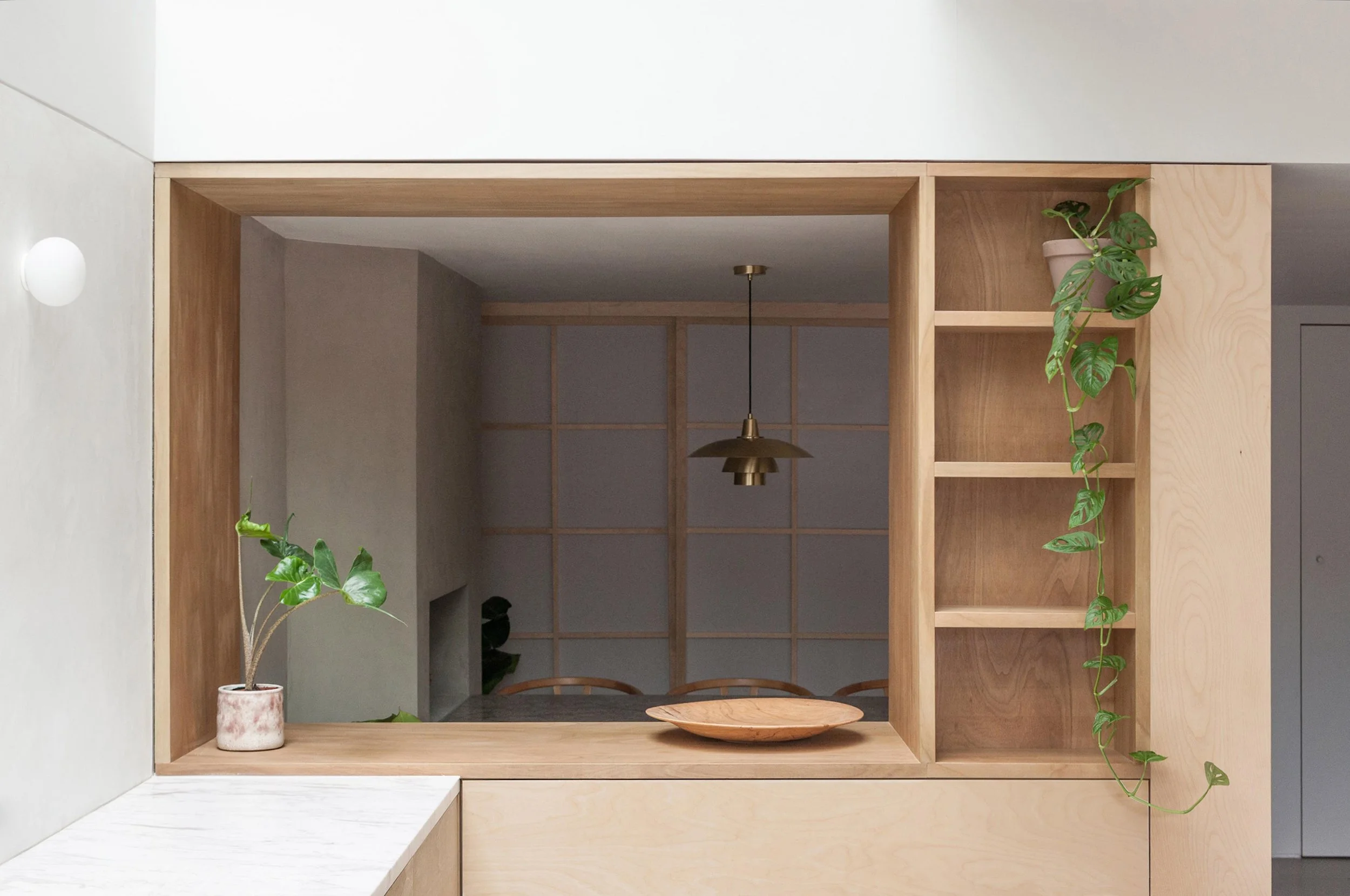 Interior view of a modern room with wooden shelving, a potted plant, and a decorative wooden bowl, visible through a large open square window.