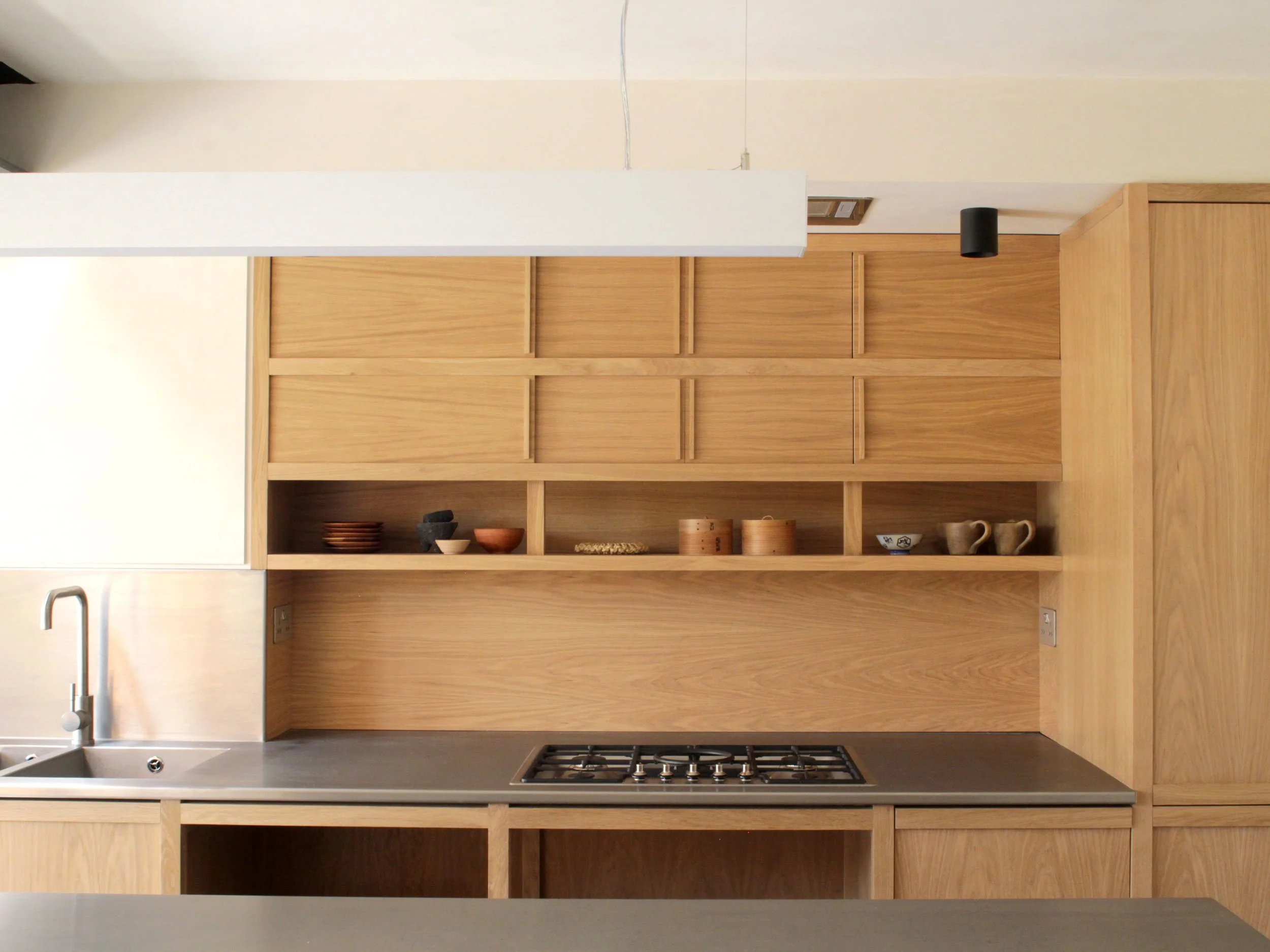 Kitchen with wooden shelves, a gray countertop, a built-in stove, and a sink with a silver faucet.