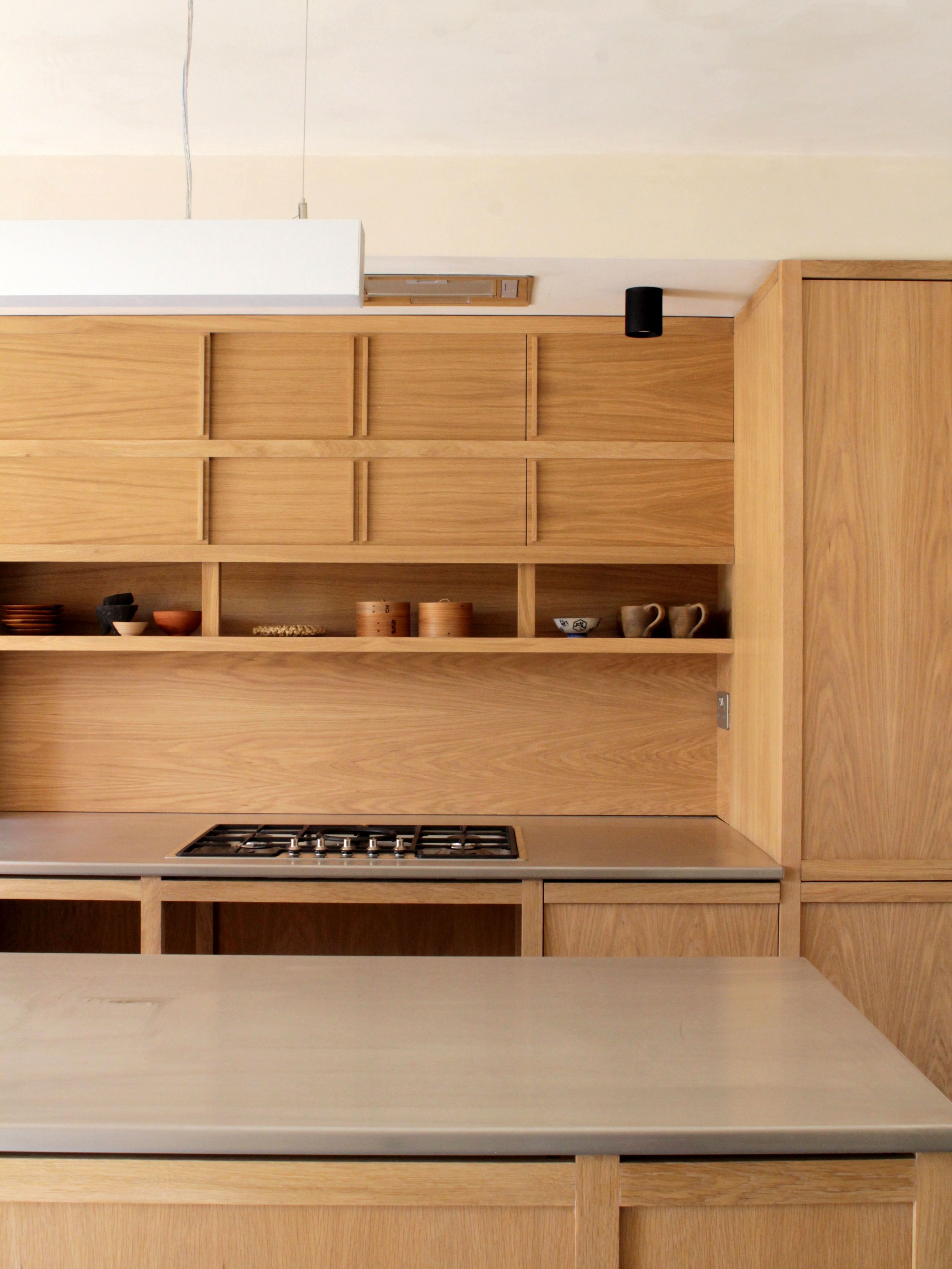 A modern kitchen with wooden cabinets, a stainless steel countertop, a gas stove, and open shelving displaying dishes and bowls.