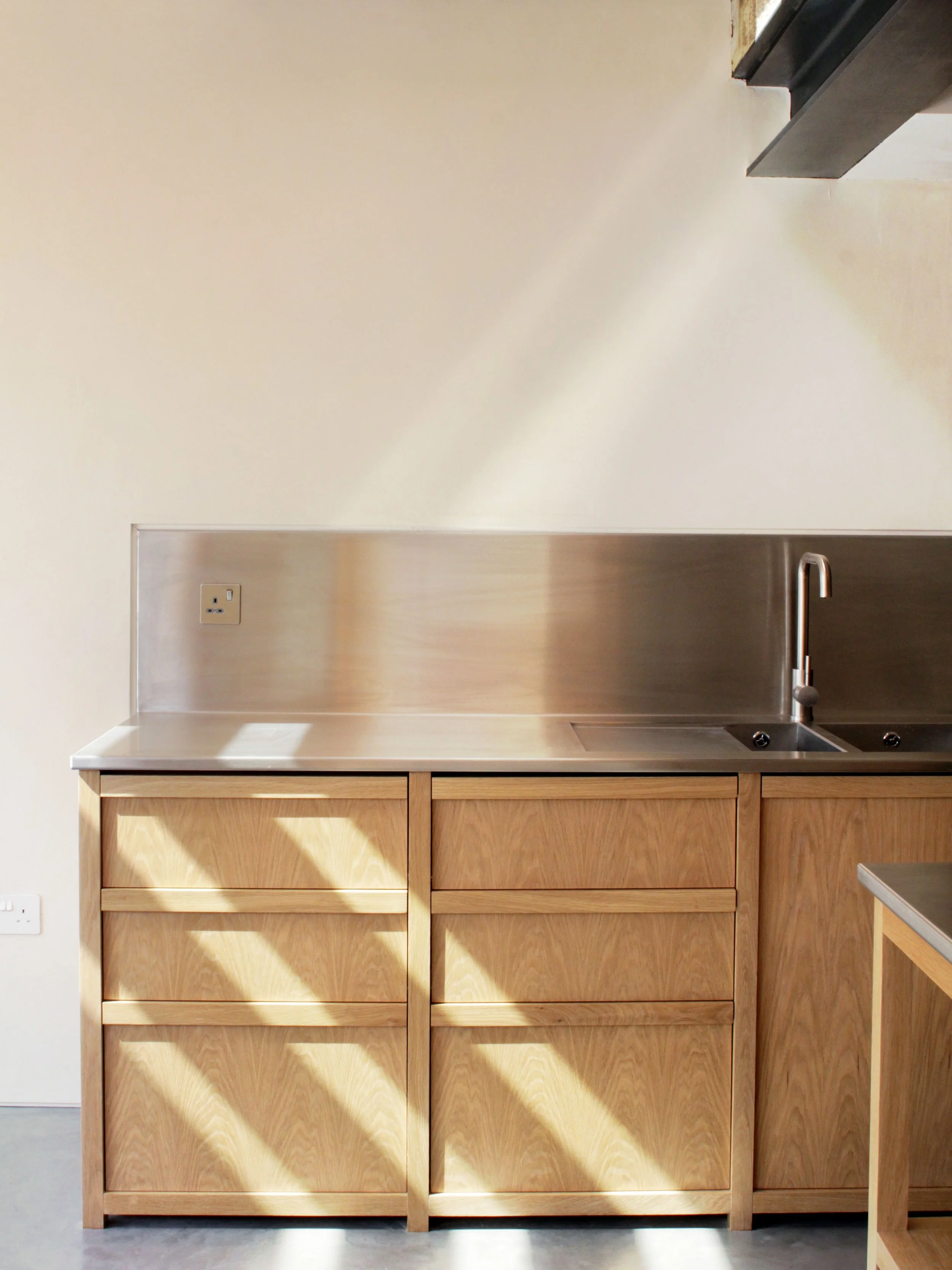 Modern kitchen with wooden cabinets, stainless steel sink, and faucet, illuminated by sunlight.