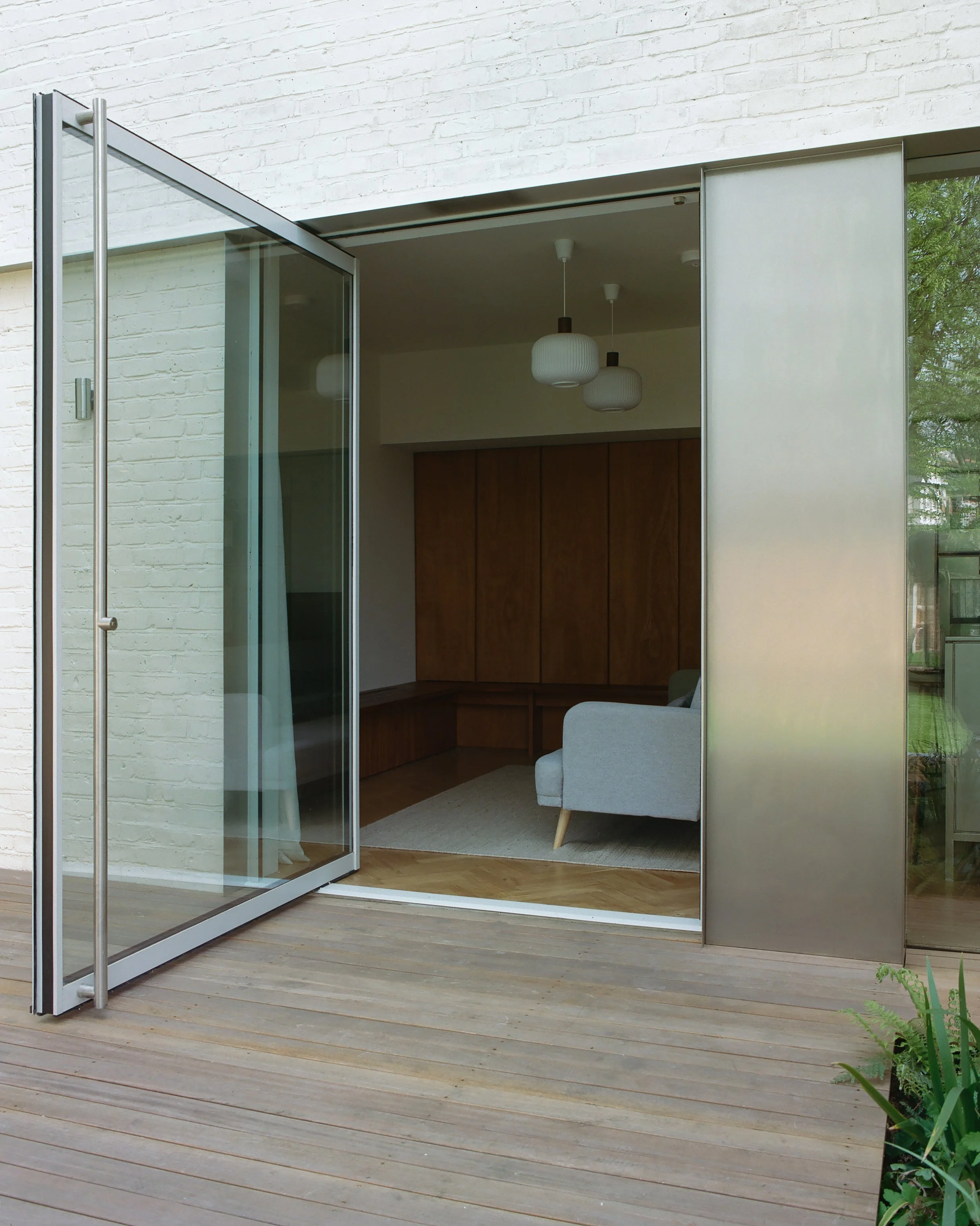 Open glass door leading to a modern living room with wooden furniture and hanging pendant lights.