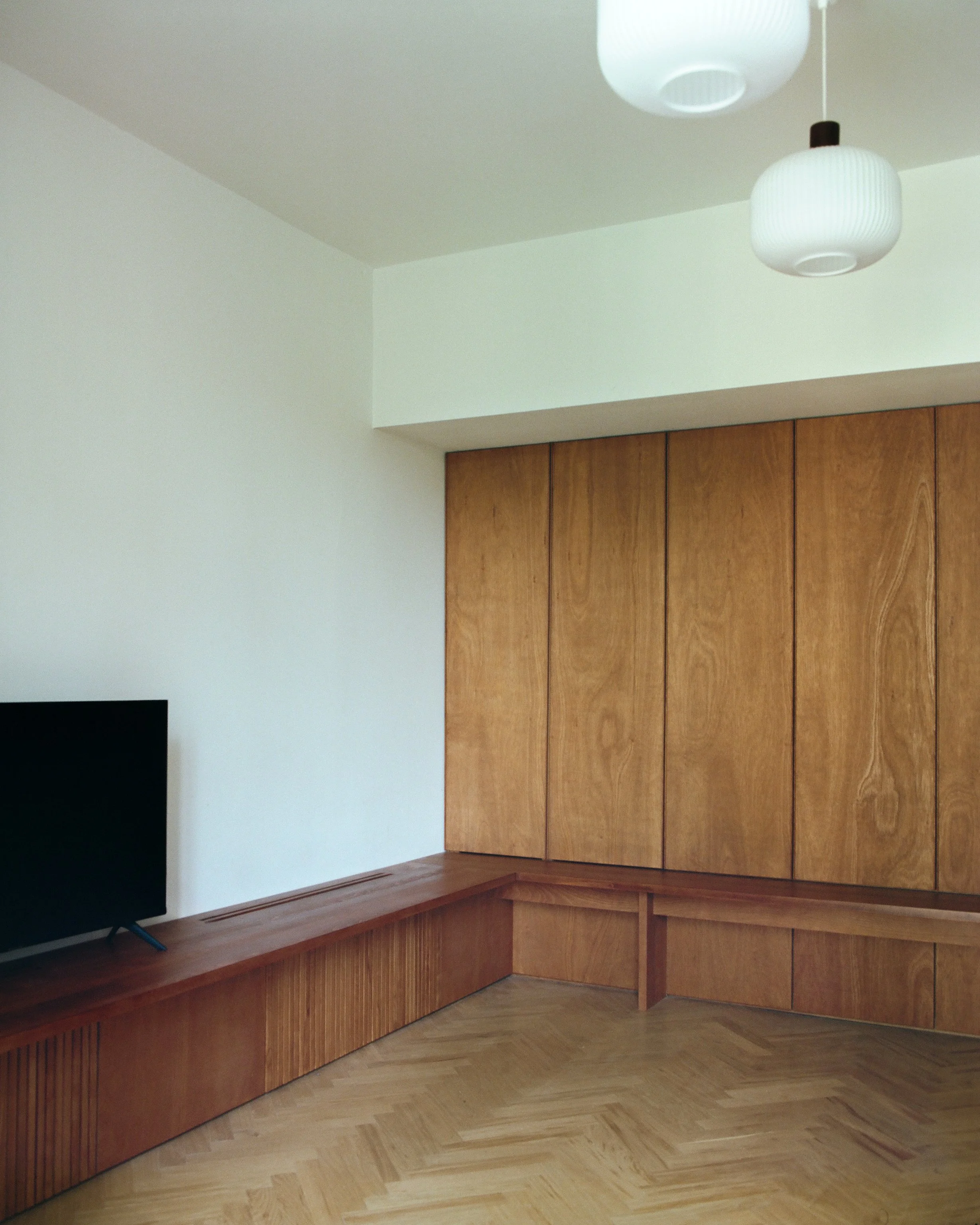Empty room with white walls, wood paneling, a wooden bench, a flat-screen TV, and white ceiling lights.