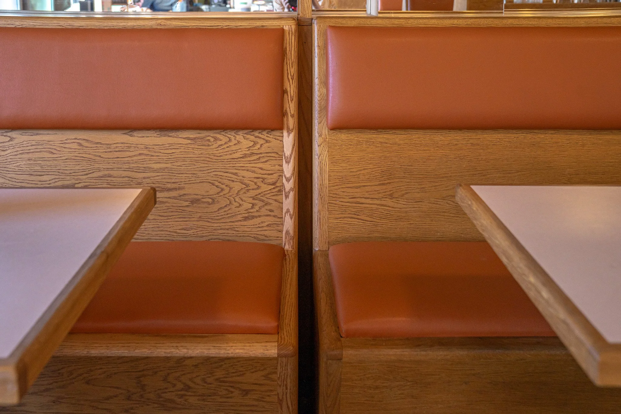 Two booths with wooden panels and orange cushioned seats, separated by a vertical wooden divider, with tables in front.