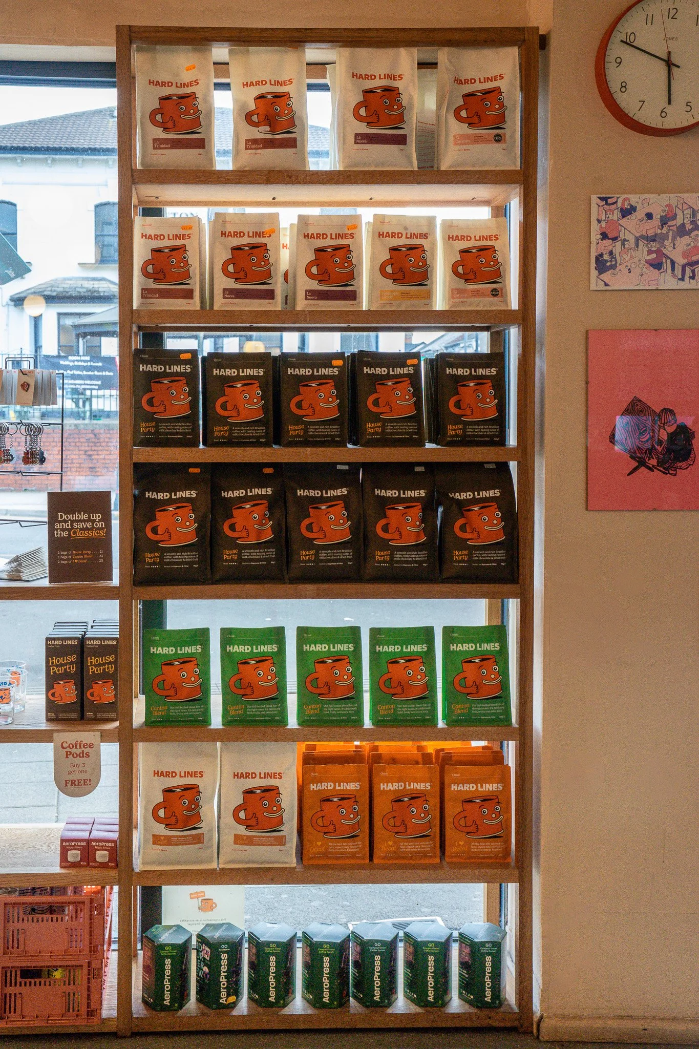 Shelf displaying various bags of Hard Lines coffee in different colors, with a clock on the wall.