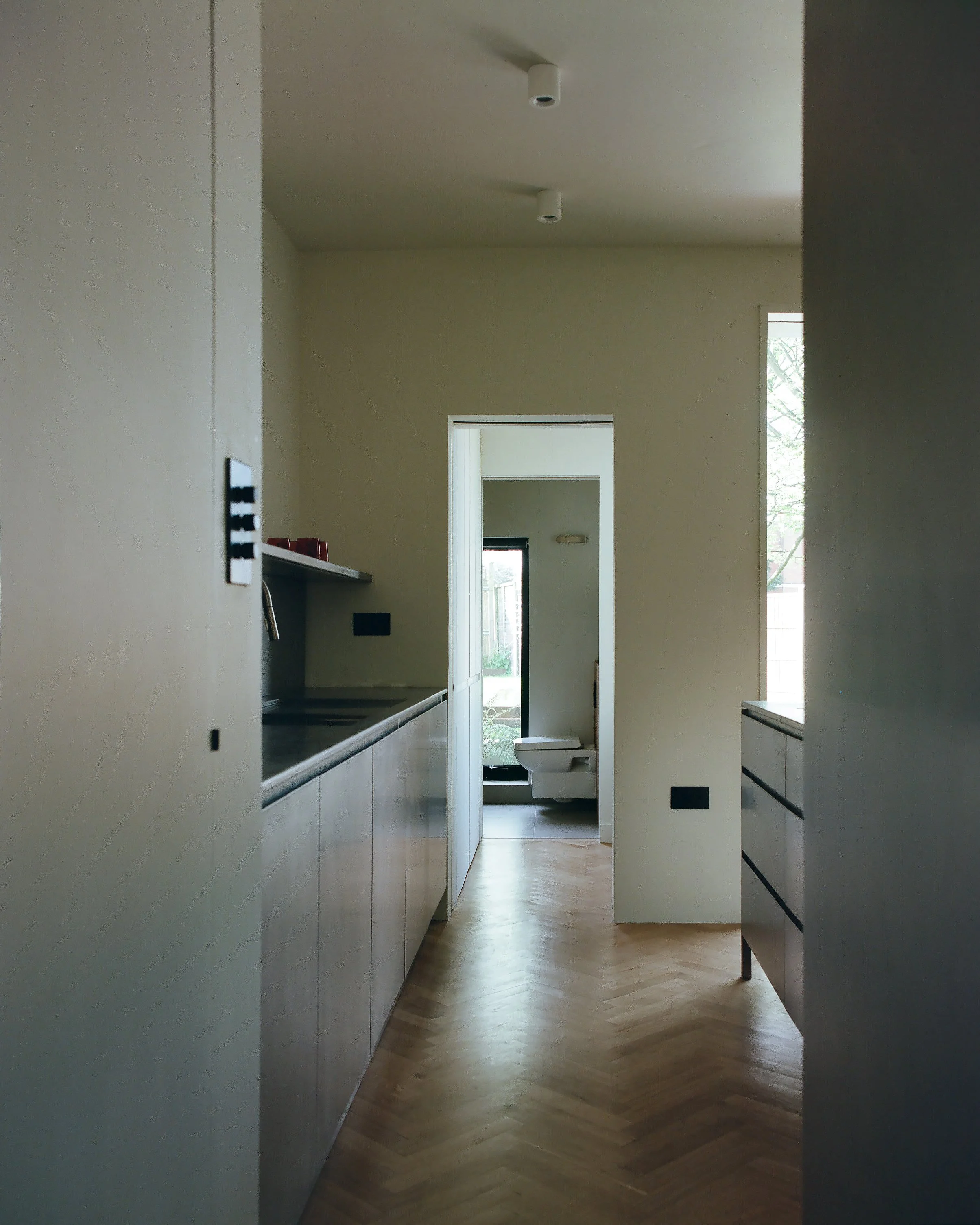 View through a kitchen into a bathroom with a toilet and window.