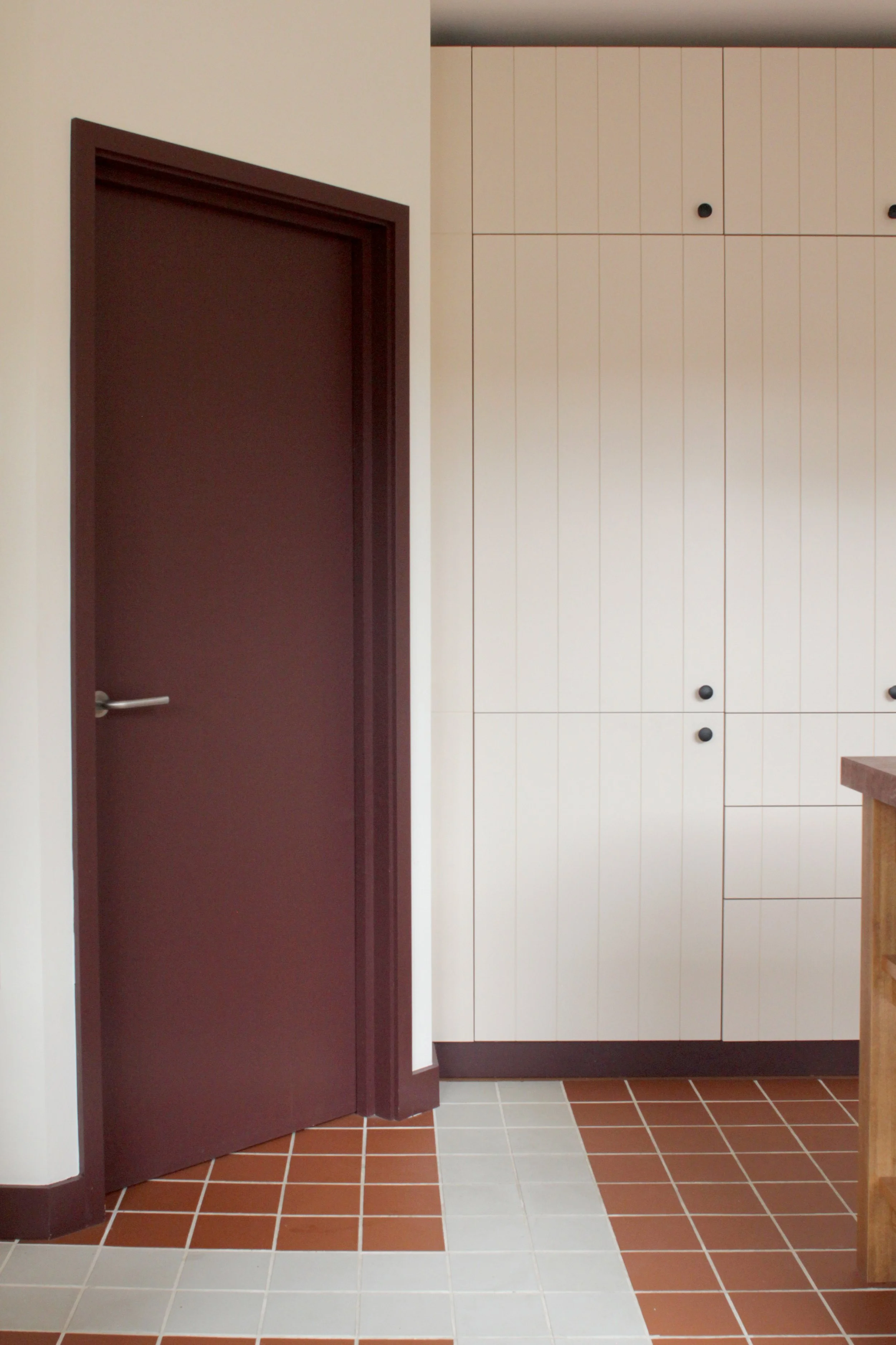 Interior of a room showing a closed purple door on the left and beige cabinets with black knobs on the right, with a tiled floor.