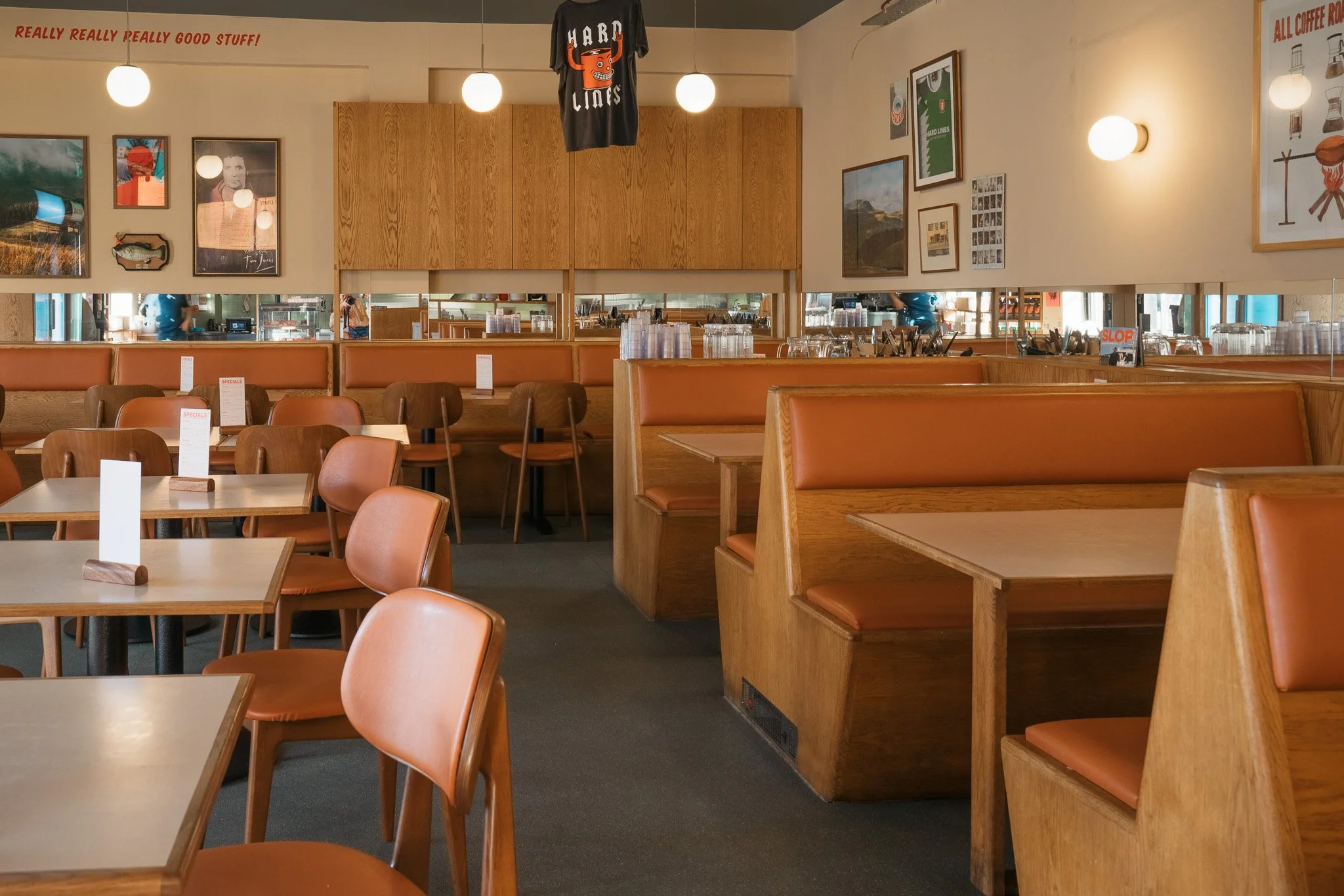 Interior of a casual restaurant with wooden furniture, booths, and wall art, illuminated by hanging and wall lights.