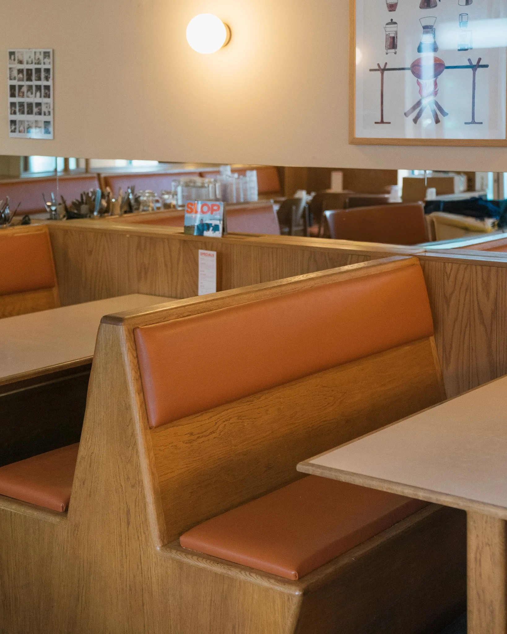 Empty booth seats with wooden frames and brown cushions in a diner. A wall with framed artwork and a mirror is visible in the background.