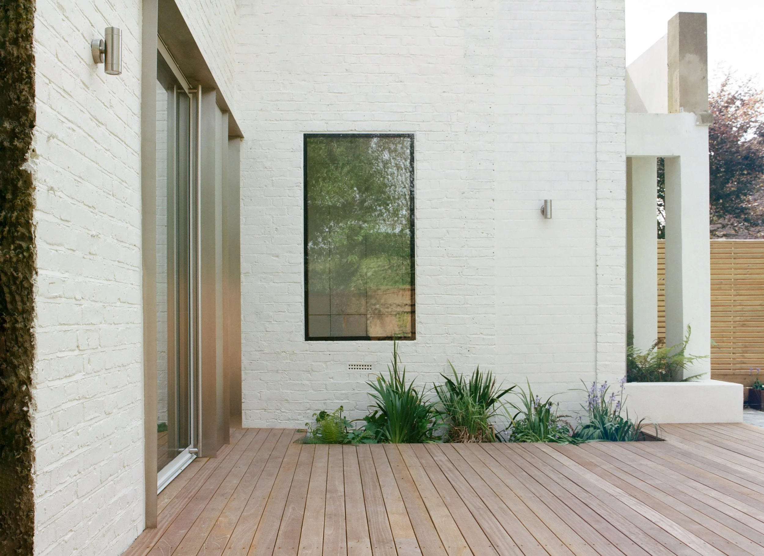 Modern white brick house with wooden deck, large window, and minimal landscaping.