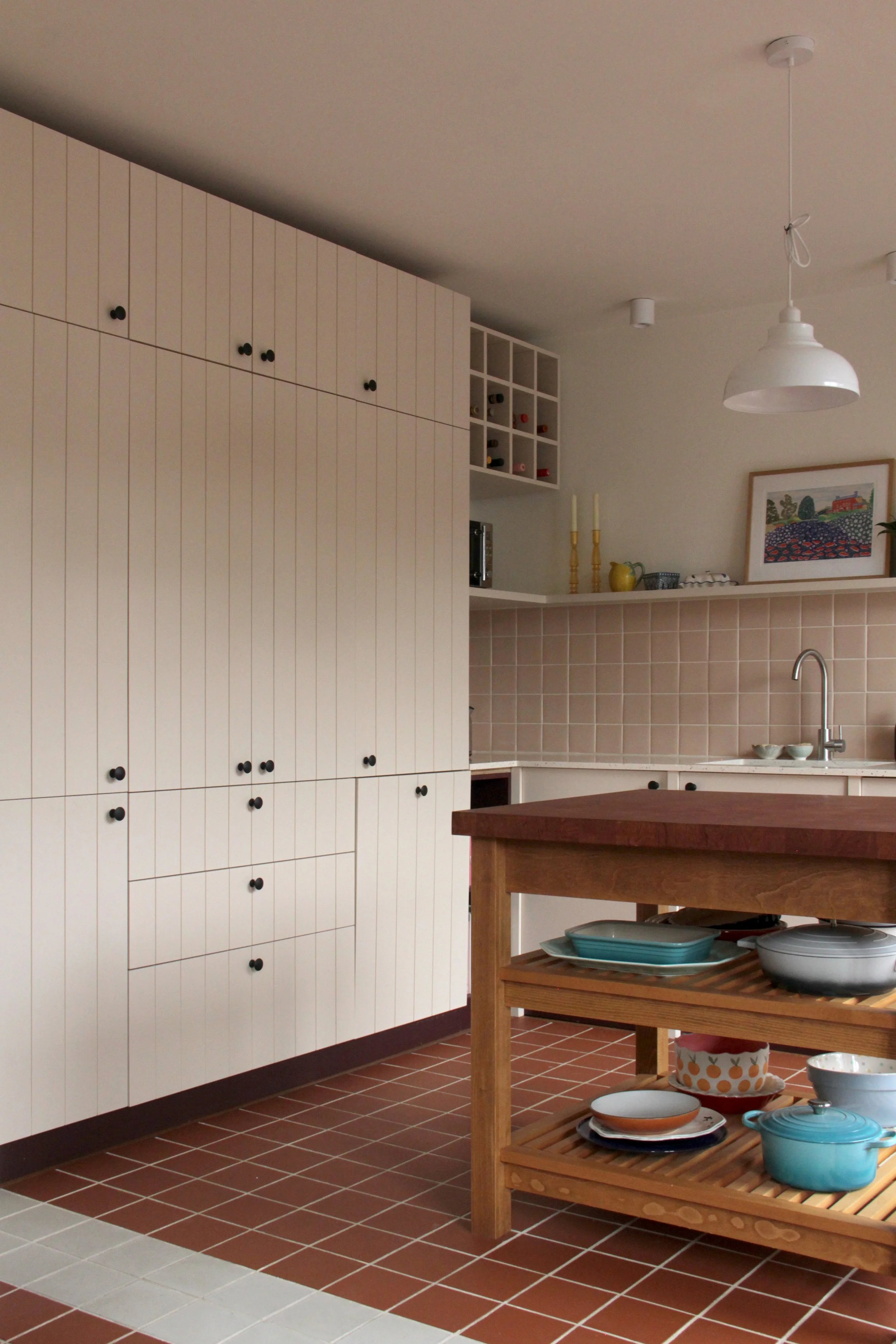 Modern kitchen with white paneled cabinets, a wooden island with kitchenware, and shelves with dishes, art, and decorative items.