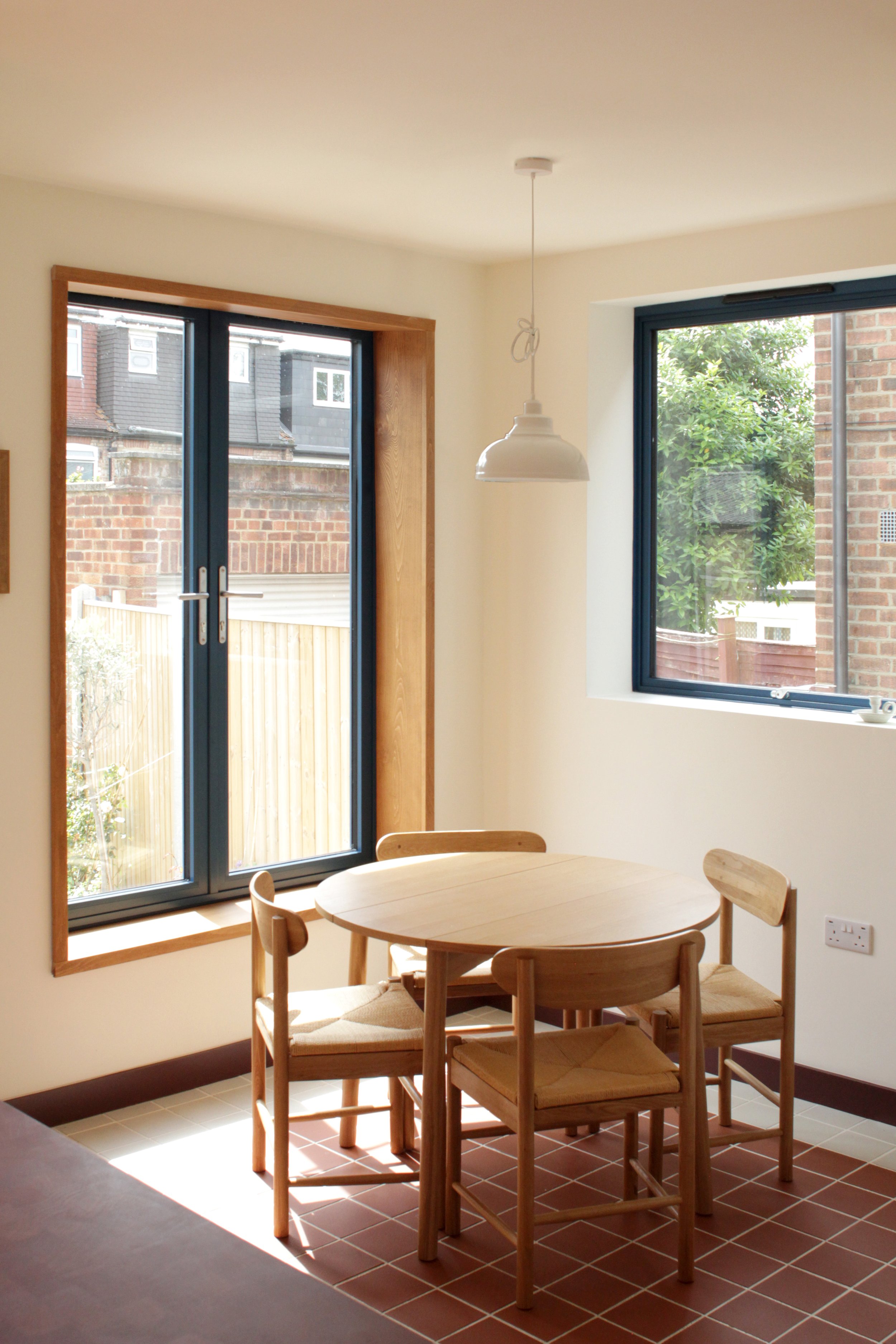 Interior of a dining area with a round wooden table, four matching chairs, two windows, and a hanging ceiling light