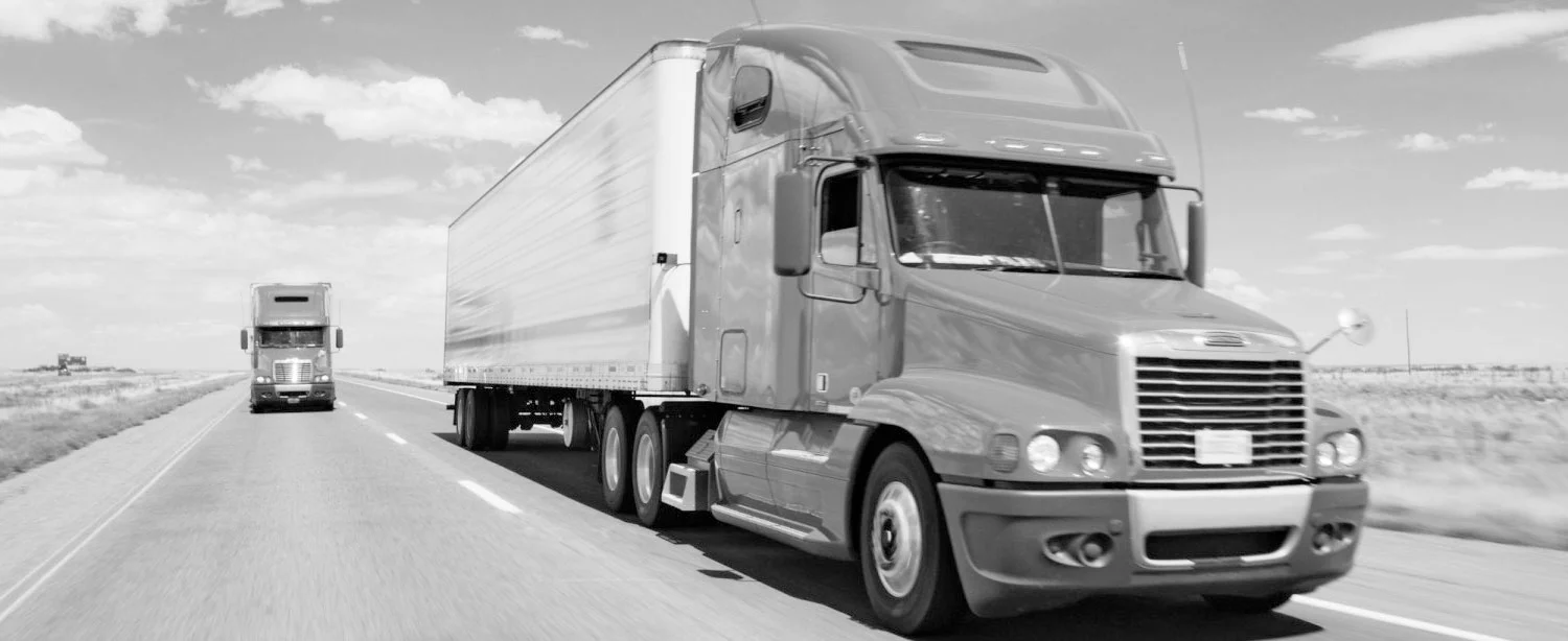 Two semi tractor-trailer trucks are driving on the highway.