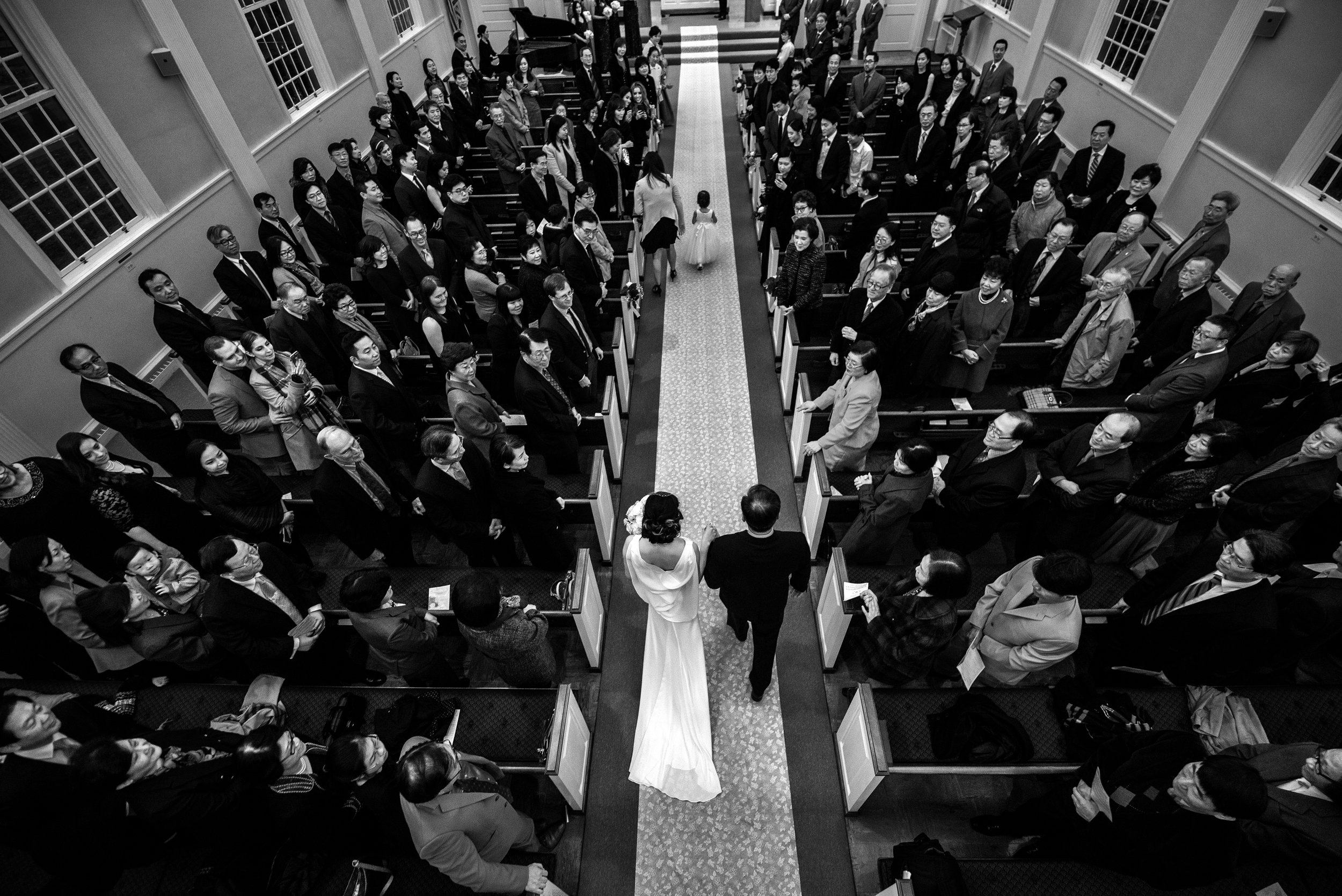 Aerial black and white shot of sustainable wedding celebration of bride escorted by father walking down the aisle of a church ceremony
