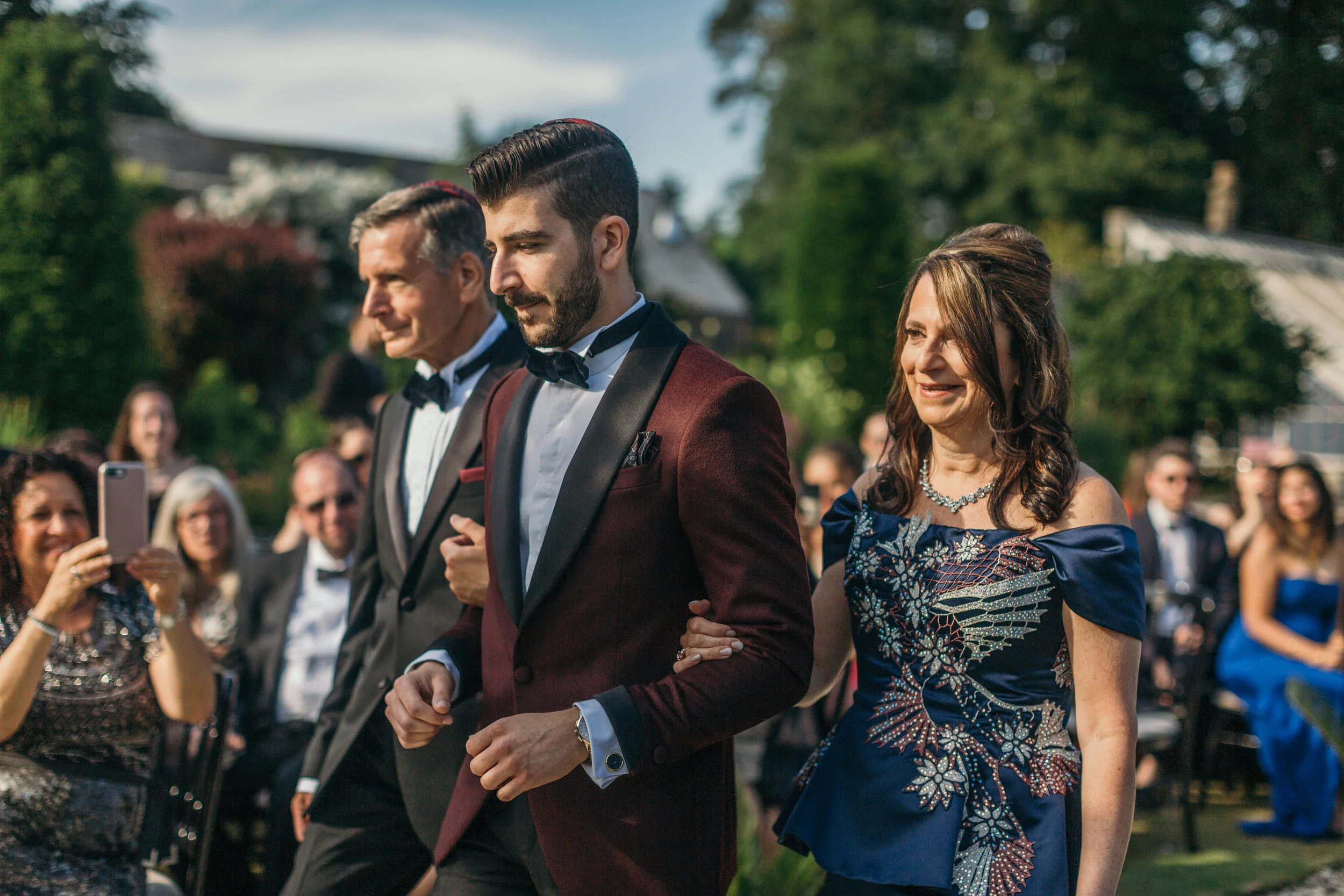Groom walking down aisle with parents in Scotland castle outdoor destination wedding
