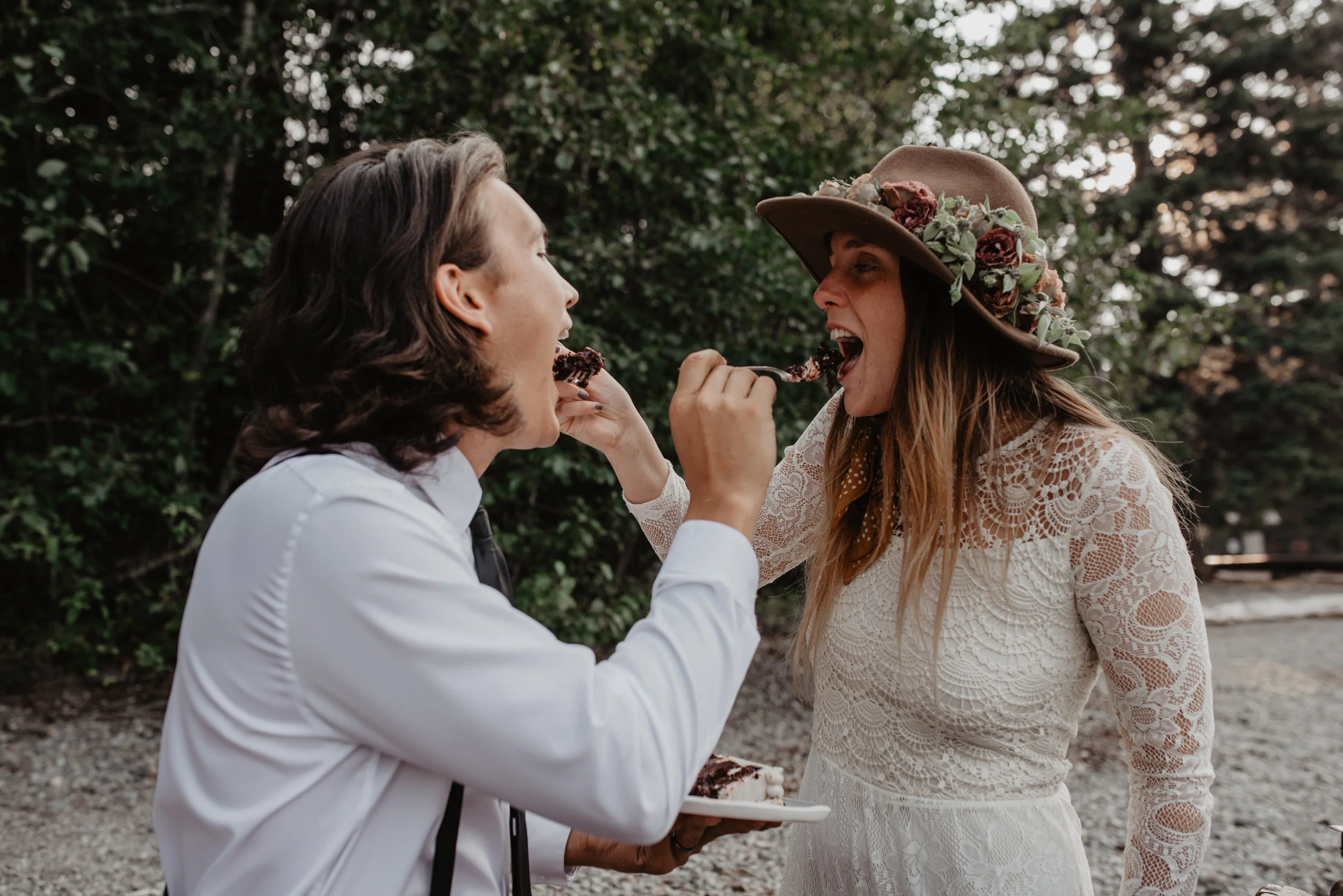 Outdoor elopement portrait of engaged couple feeding each other organic wedding cake at Glacier National Park MT