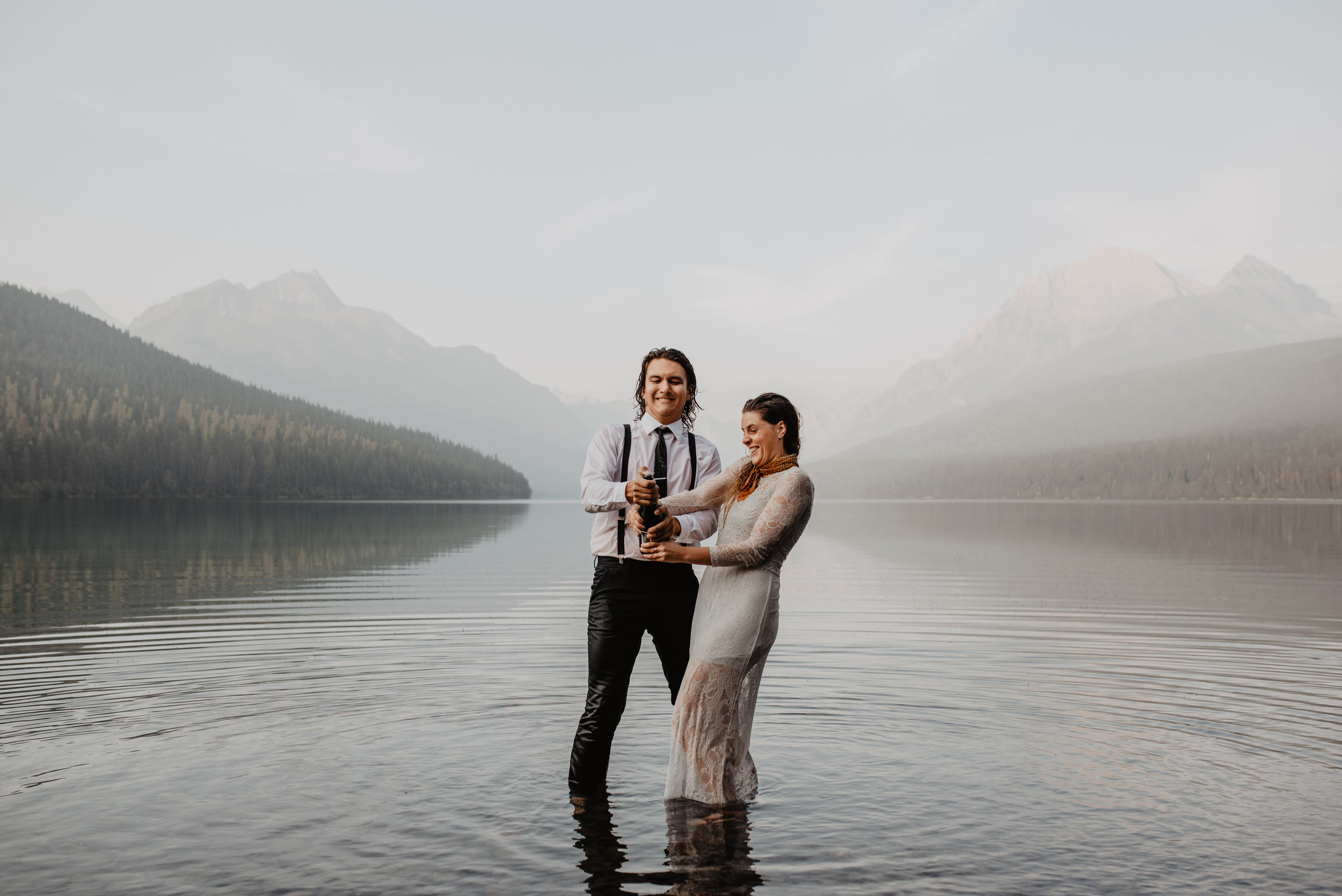 Outdoor elopement portrait of engaged couple poping champagne while in water at Glacier National Park MT